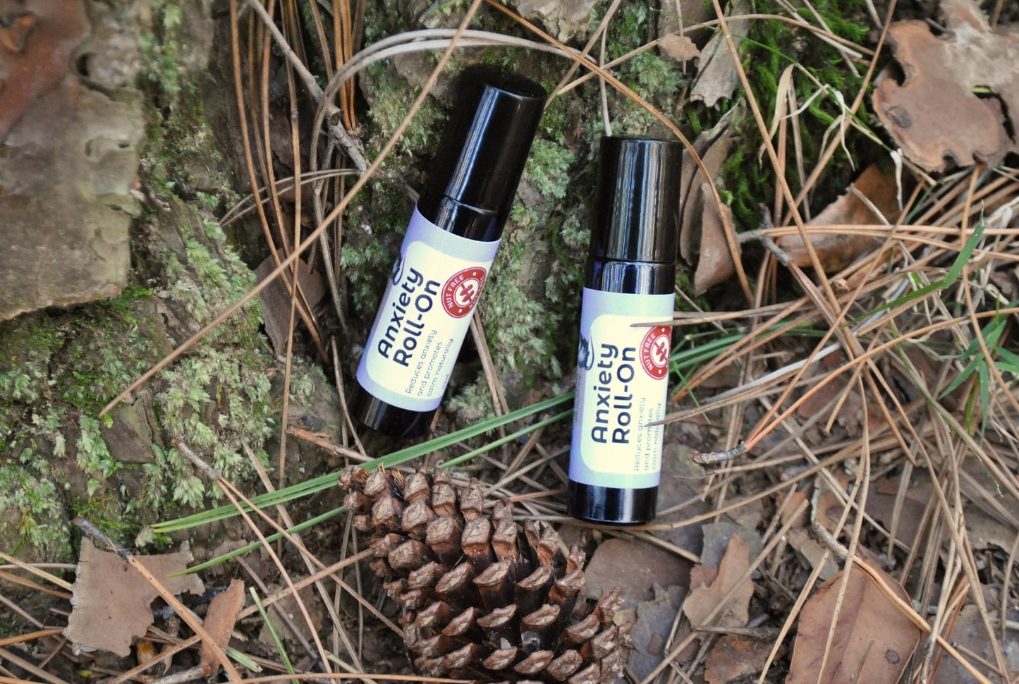Two Anxiety Roll-on bottles on a natural background with pine cones and leaves.