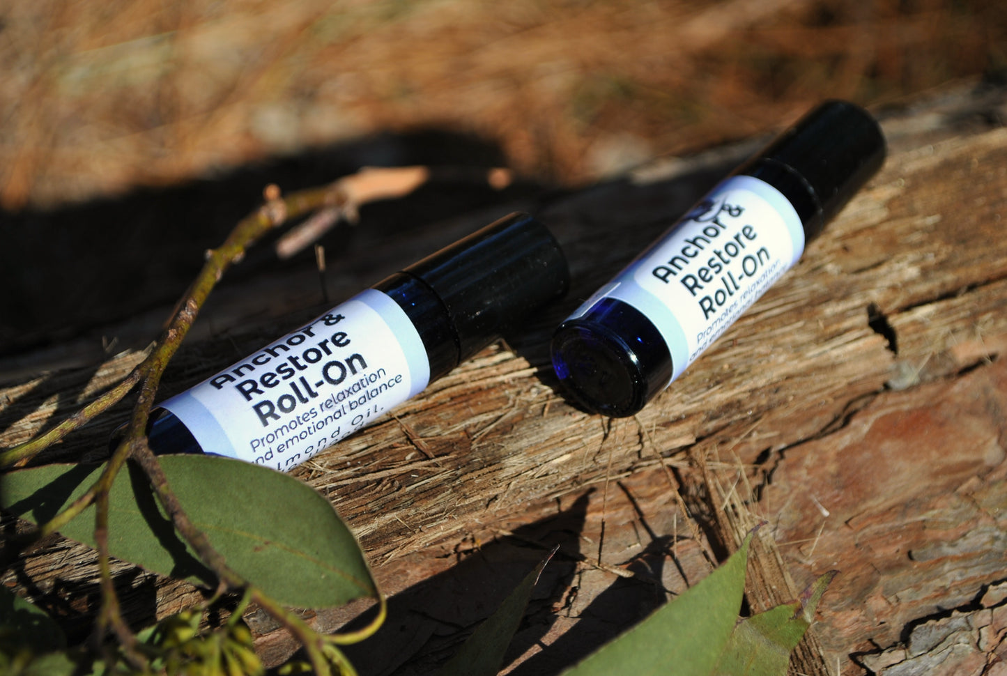 Two 'Anchor & Restore Roll-On' bottles on a wooden surface with leaves.