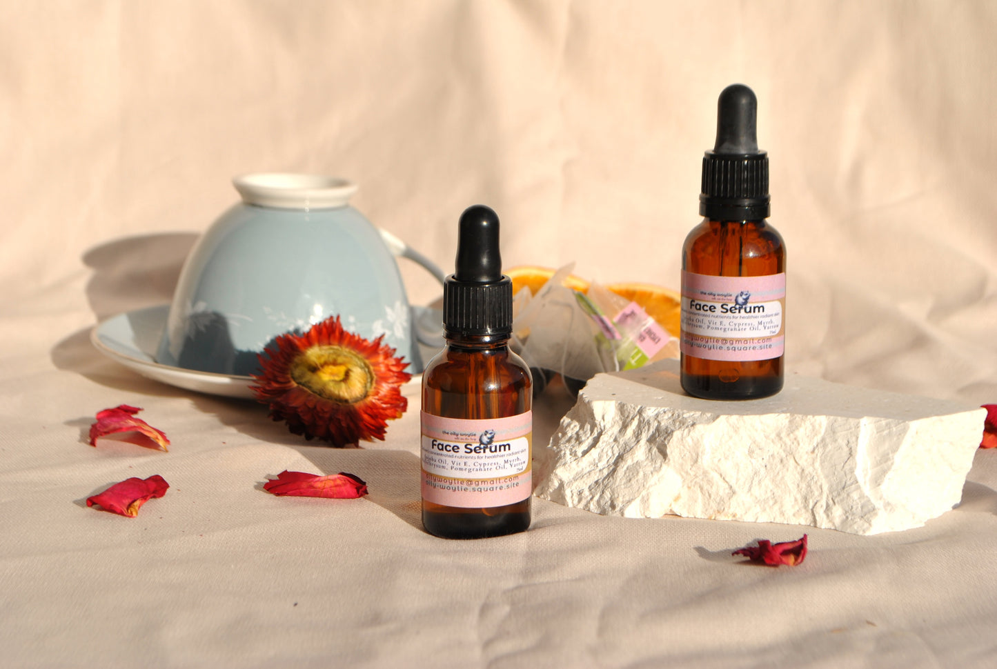 Two bottles of face serum with droppers on a textured surface with flowers and a teapot.