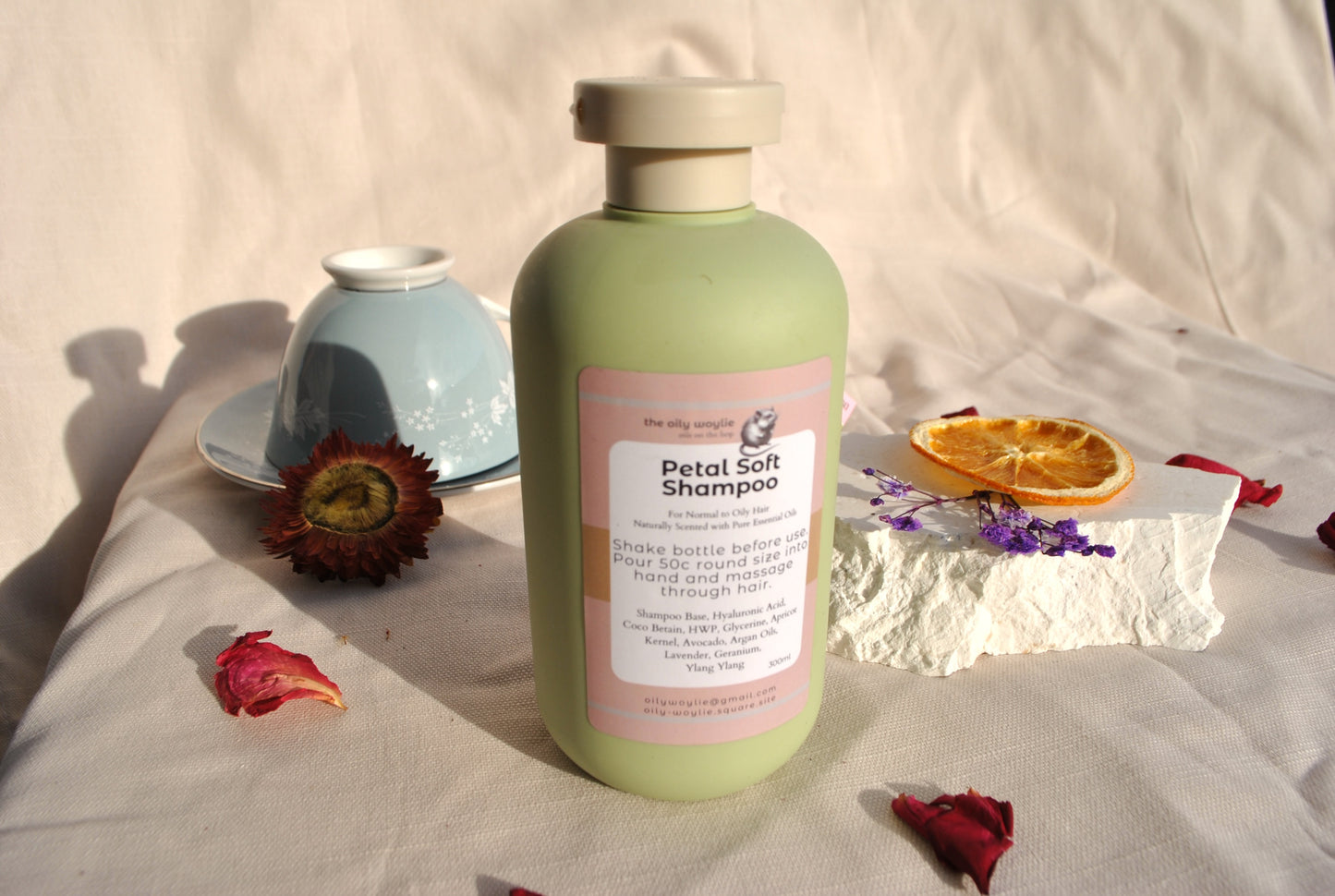 Green shampoo bottle with pink label on a textured surface with flowers and a bowl.