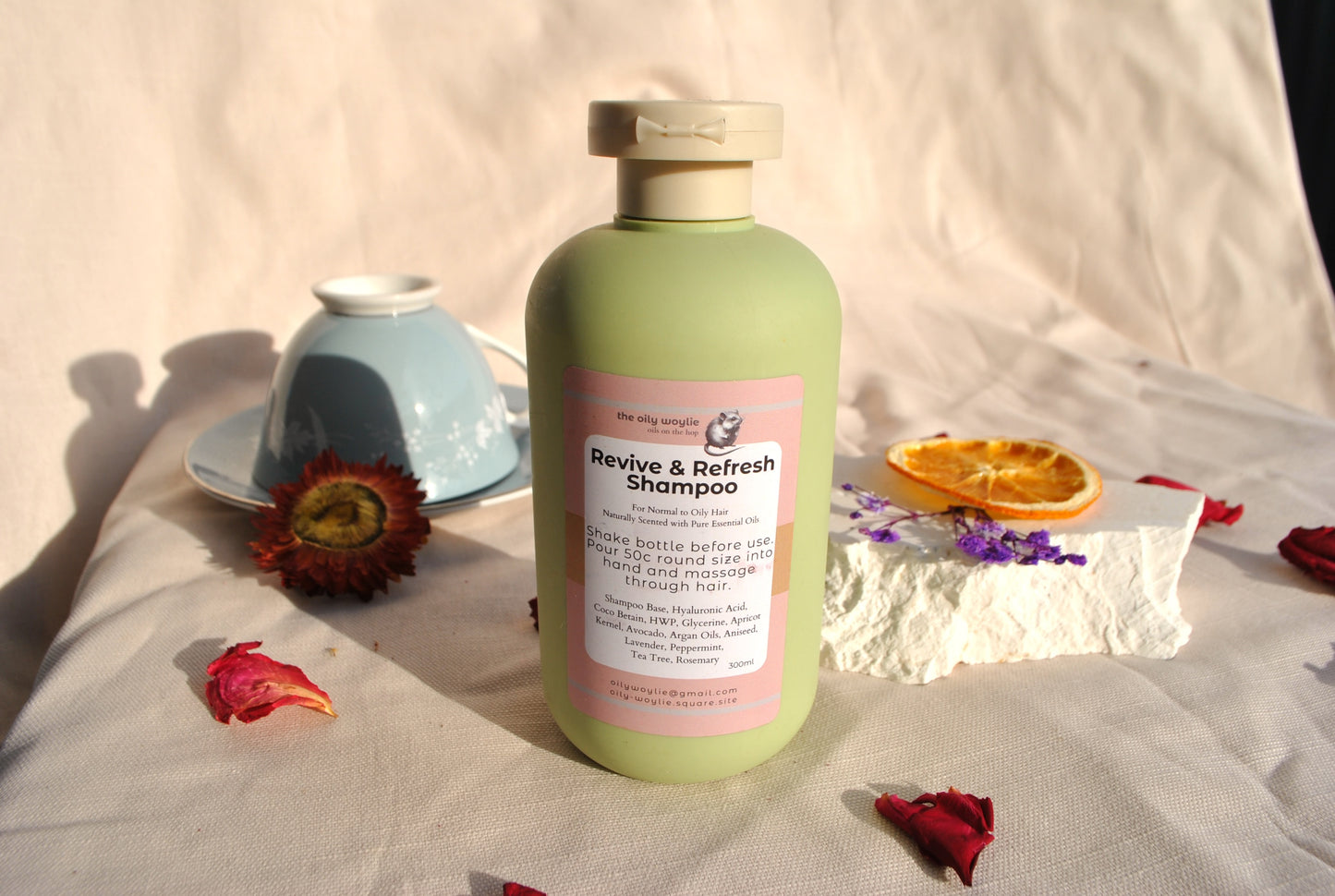 Green shampoo bottle with pink label on a light fabric background with flowers and a bowl.
