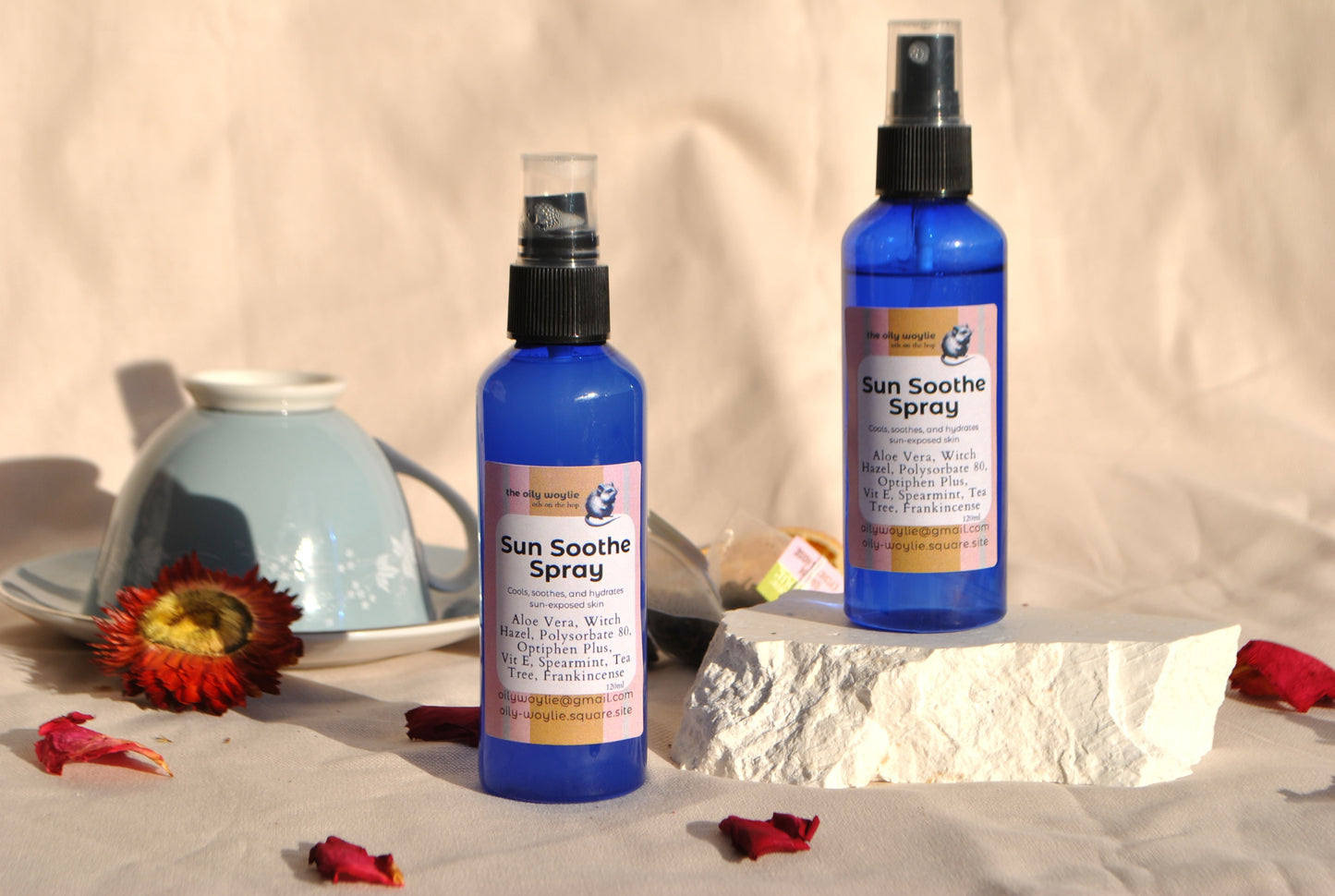 Two bottles of Sun Soothe Spray on a neutral background with flowers and a teapot.