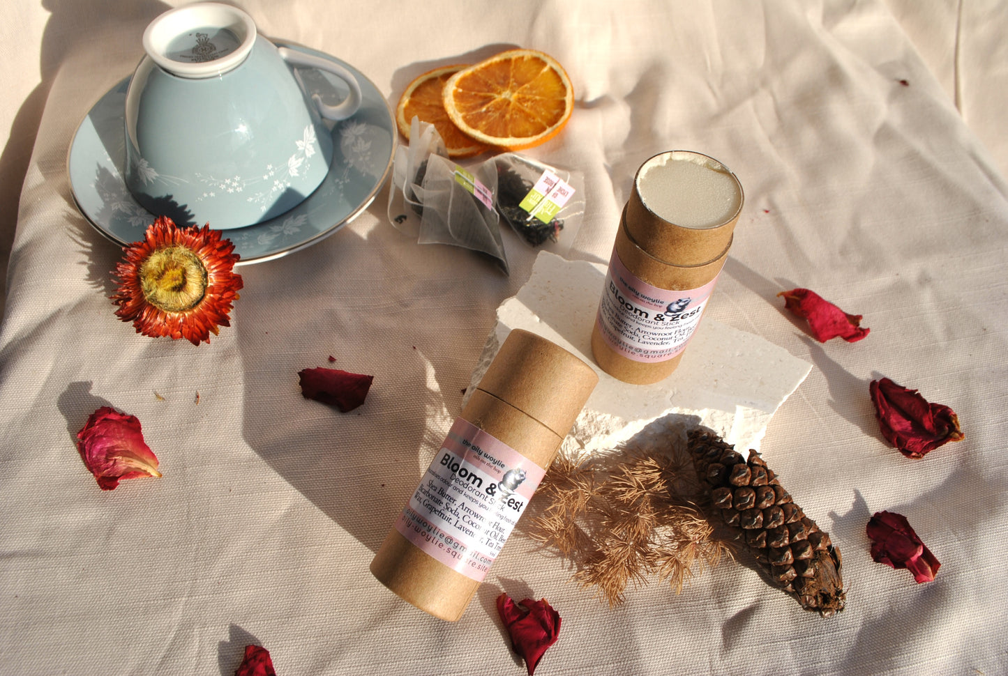 Two gold containers with labels on a textured surface with dried flowers and a teacup.