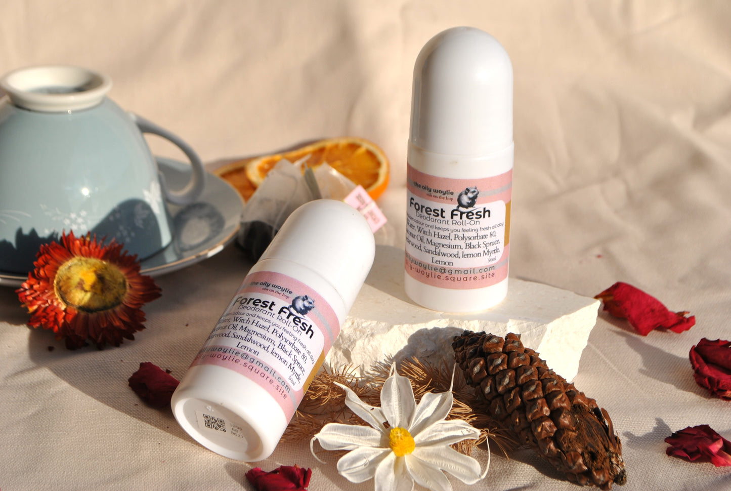 Two bottles of 'Forest Fresh' products on a textured surface with natural elements like flowers and a pine cone.