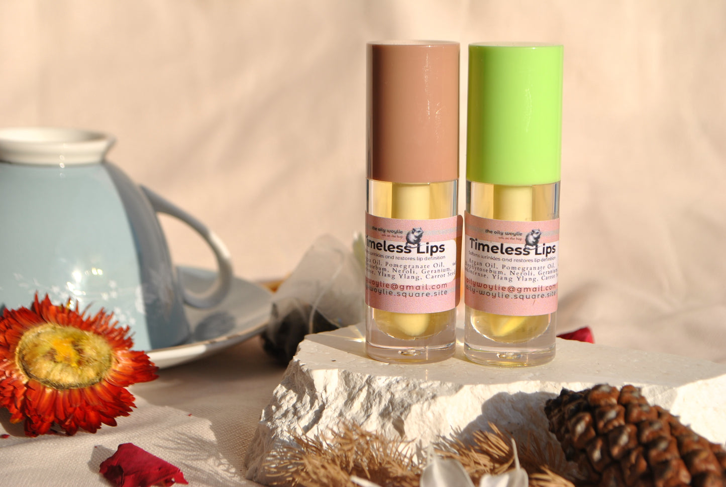 Two bottles of 'Timeless Lips' lip balm on a decorative surface with a teacup and flowers.