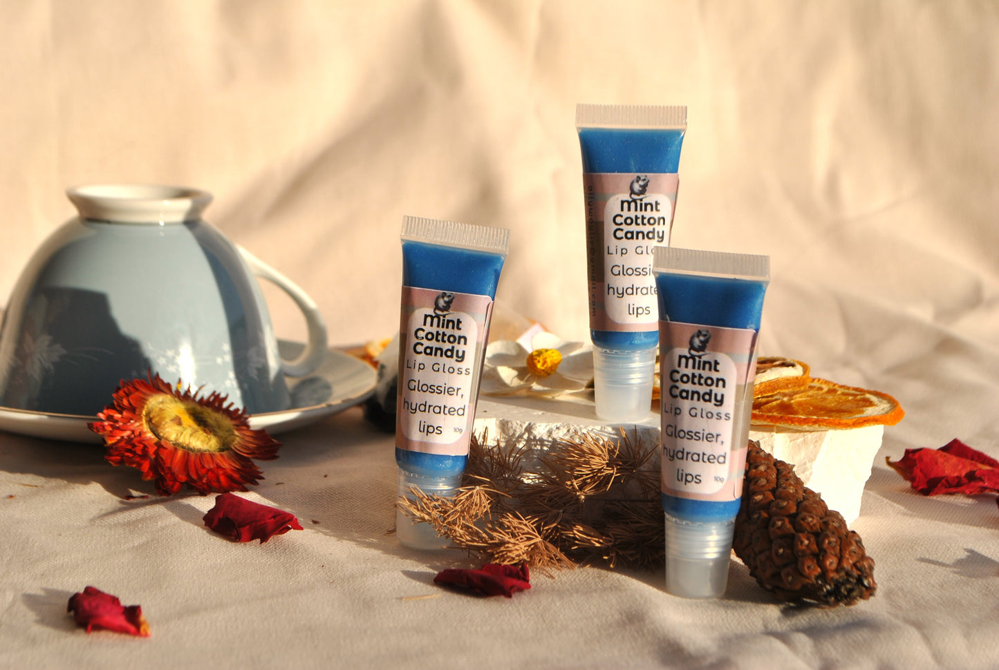 Three tubes of Mint Cotton Candy lip balm on a textured surface with decorative elements.