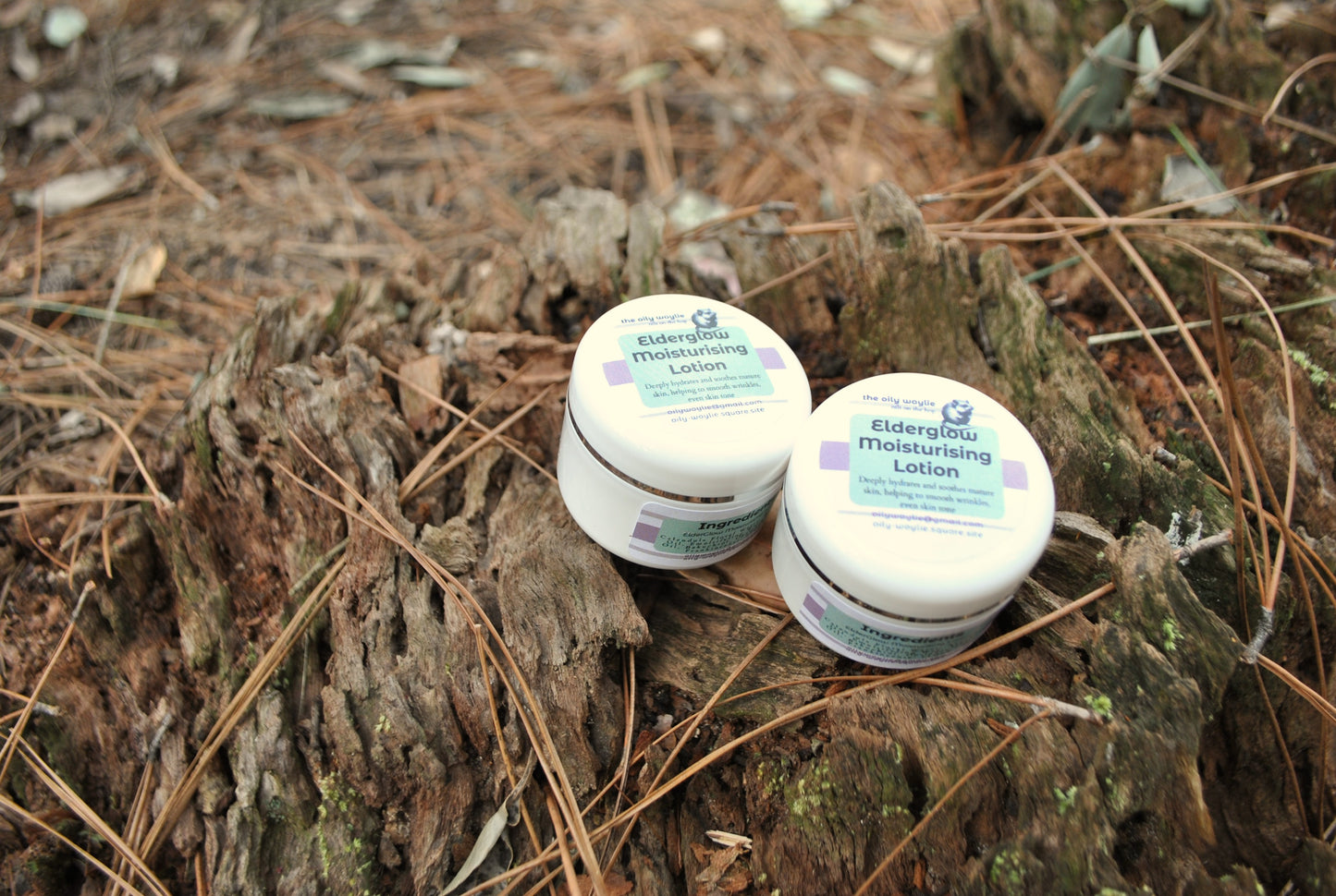 Two containers of Elderflower Throat Soothing Lotion on a wooden surface with pine needles.