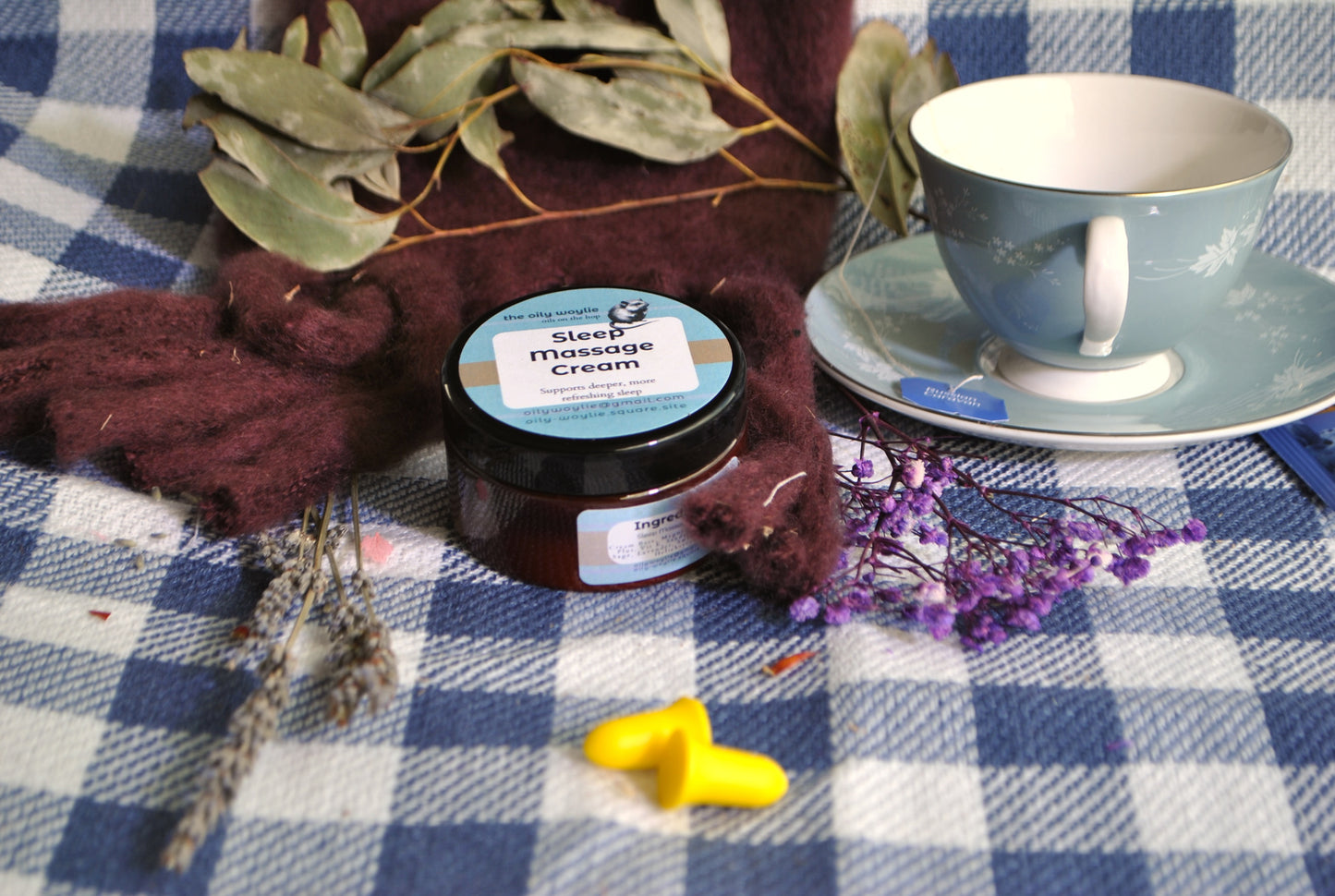 Jar of sleep massage cream on a checkered tablecloth with a teacup and decorative elements.