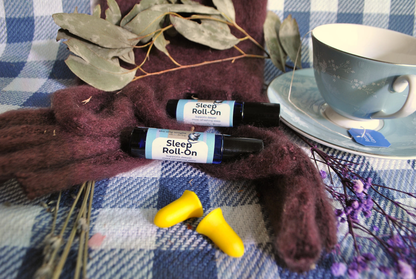 Sleep Roll-On bottles with earplugs and a cup on a checkered tablecloth.