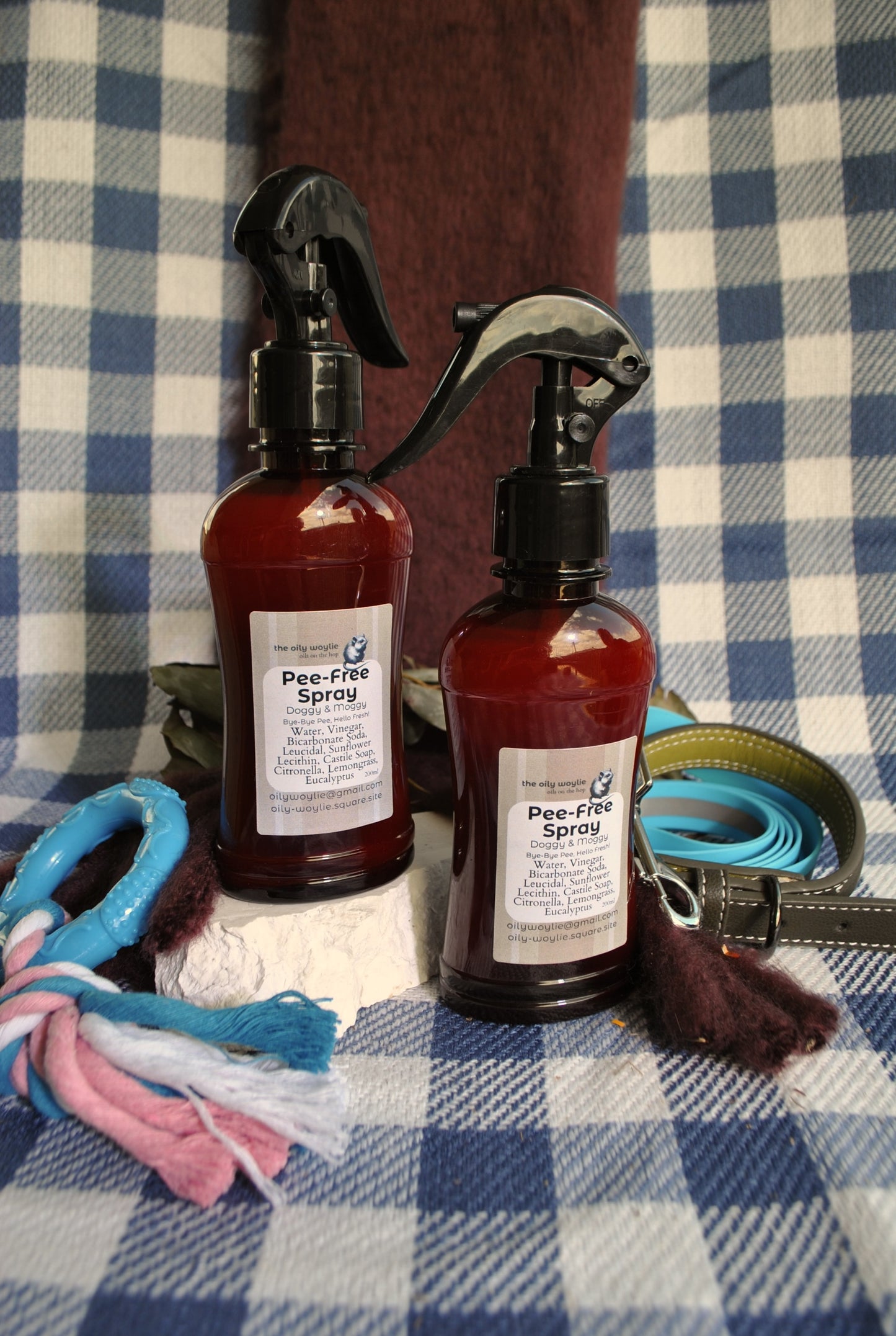 Two bottles of 'Pee-Free Spray' on a checkered fabric background with dog accessories.