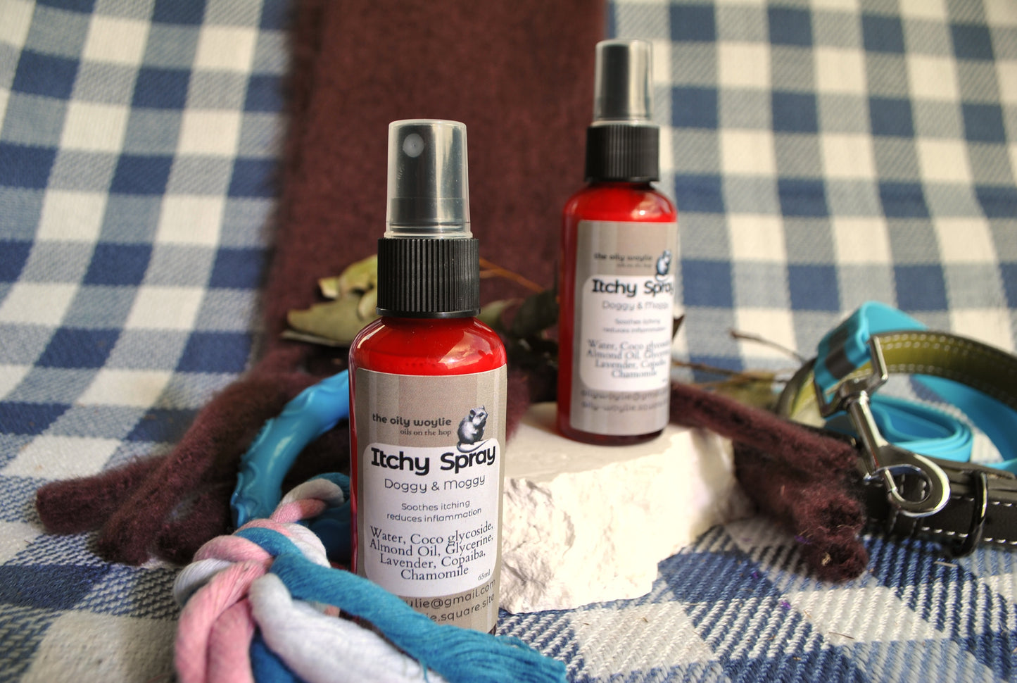 Two bottles of 'Itchy Spray' on a checkered fabric background with pet accessories.
