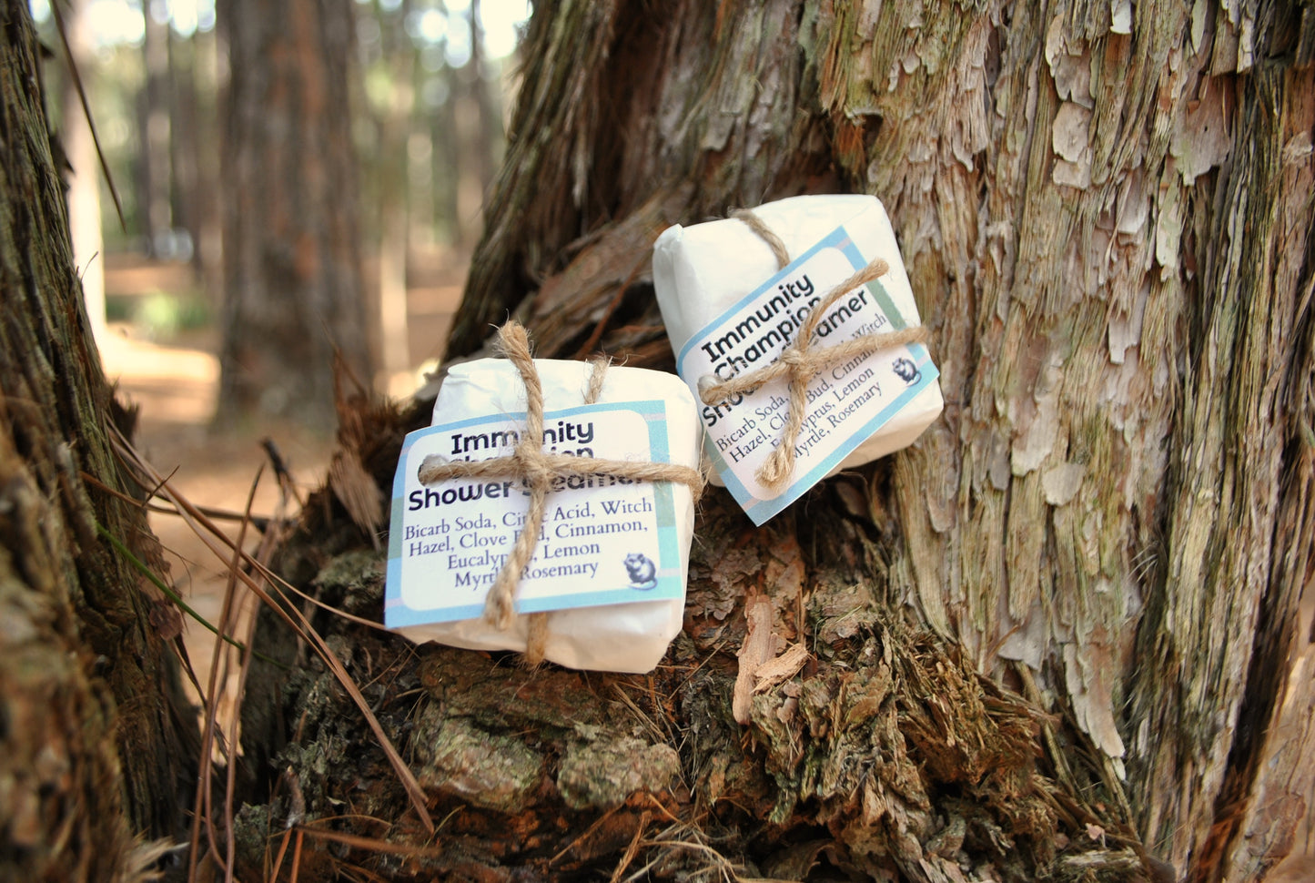Two shower steamers labeled 'Immunity' hanging from a tree branch in a forest setting.