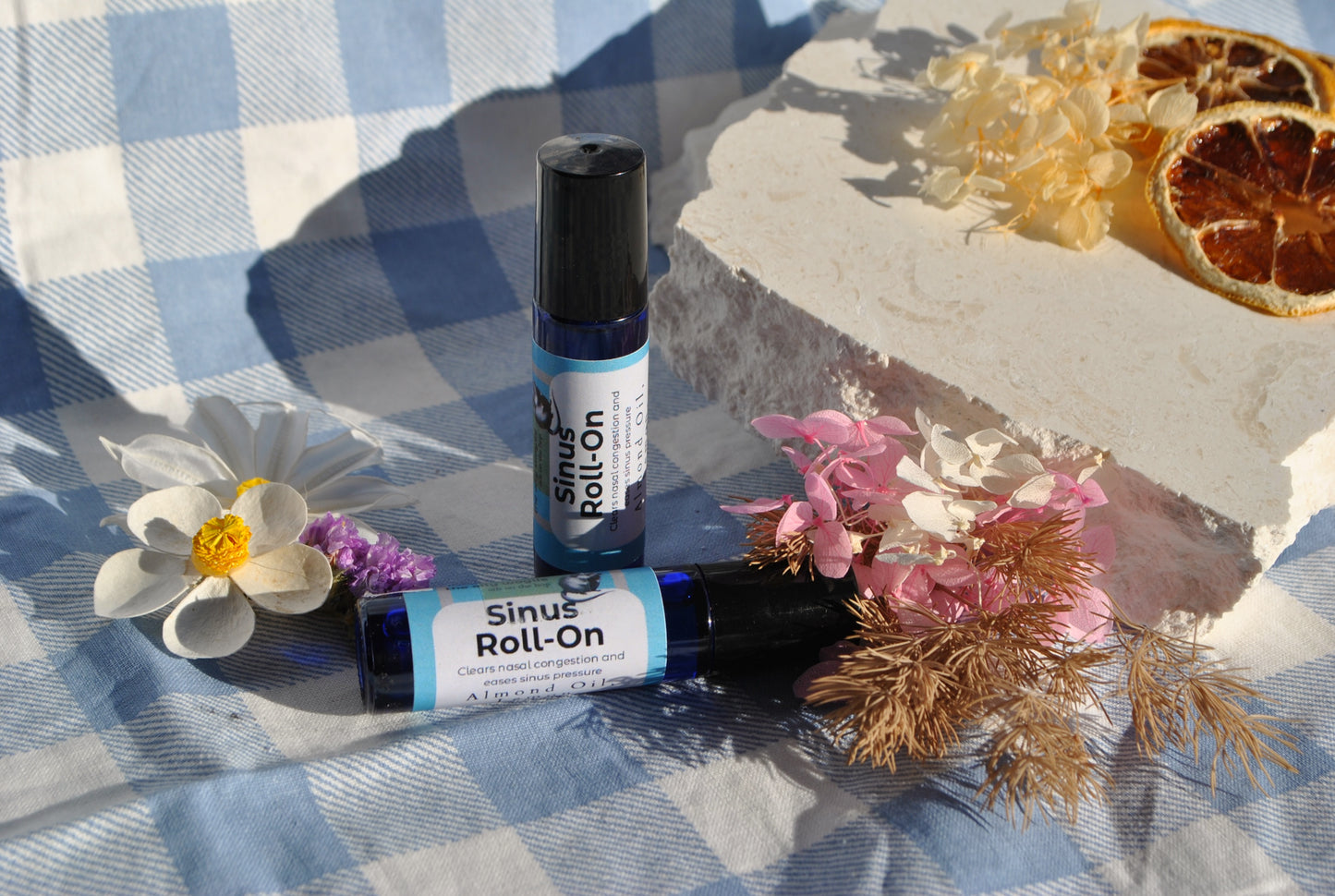 Two bottles of Sinus Roll-On with flowers on a checkered fabric background
