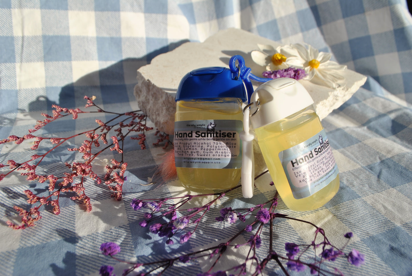 Two bottles of hand sanitizer on a checkered tablecloth with flowers and branches.