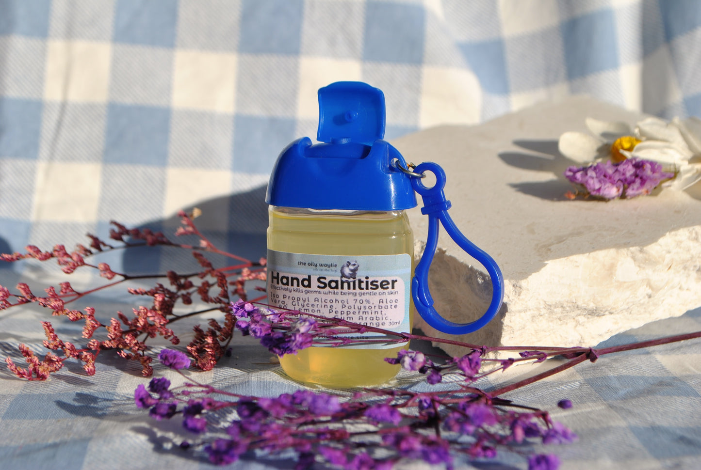Hand sanitiser bottle with blue cap and keychain on a checkered fabric background with flowers.