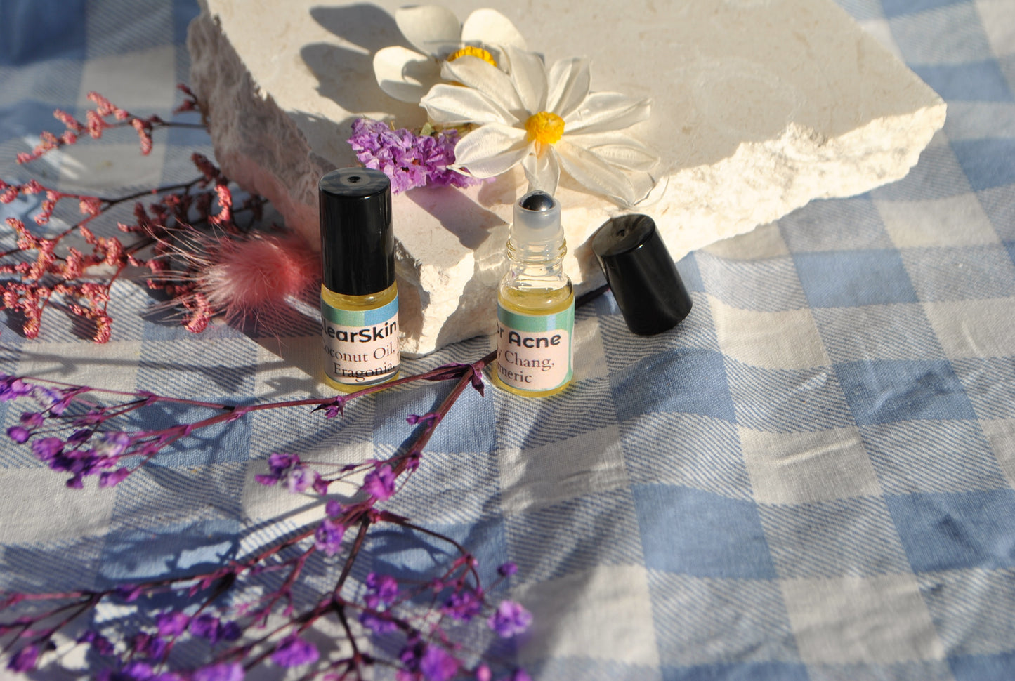 Two small bottles of skincare products on a checkered fabric background with flowers and feathers.