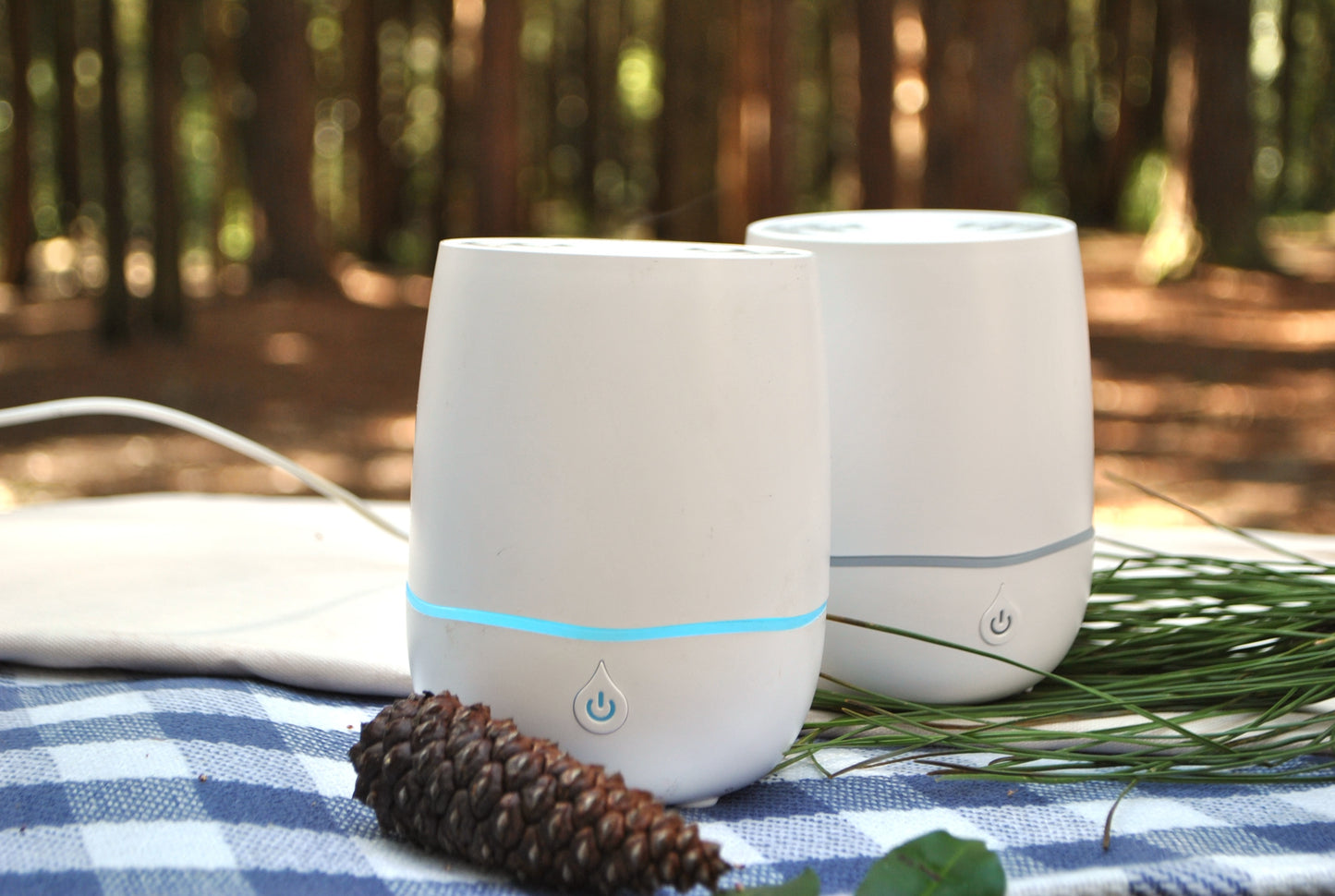 Two white humidifiers with blue lights on a table outdoors, surrounded by nature.
