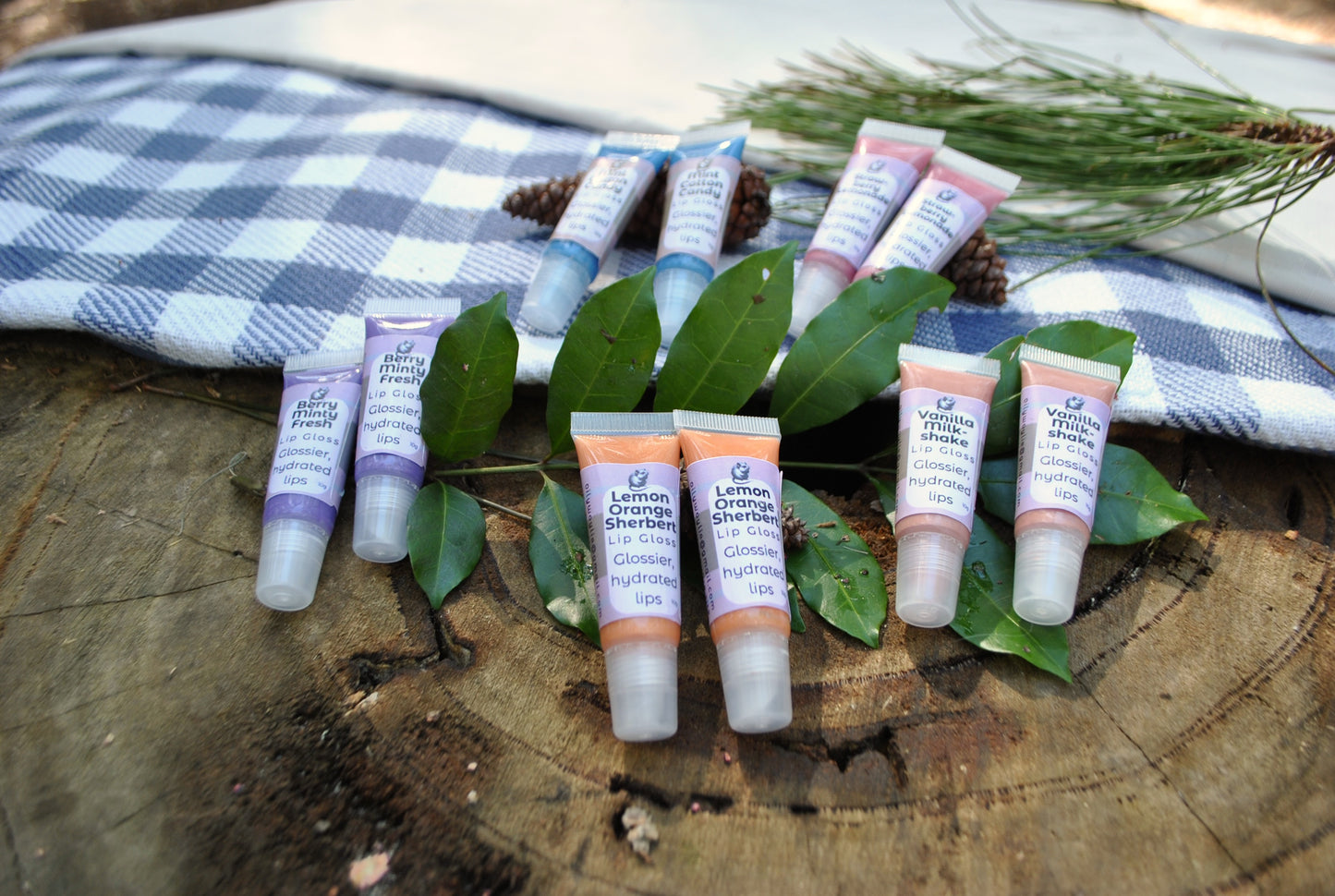 Lip gloss tubes on green leaves with a checkered cloth in the background