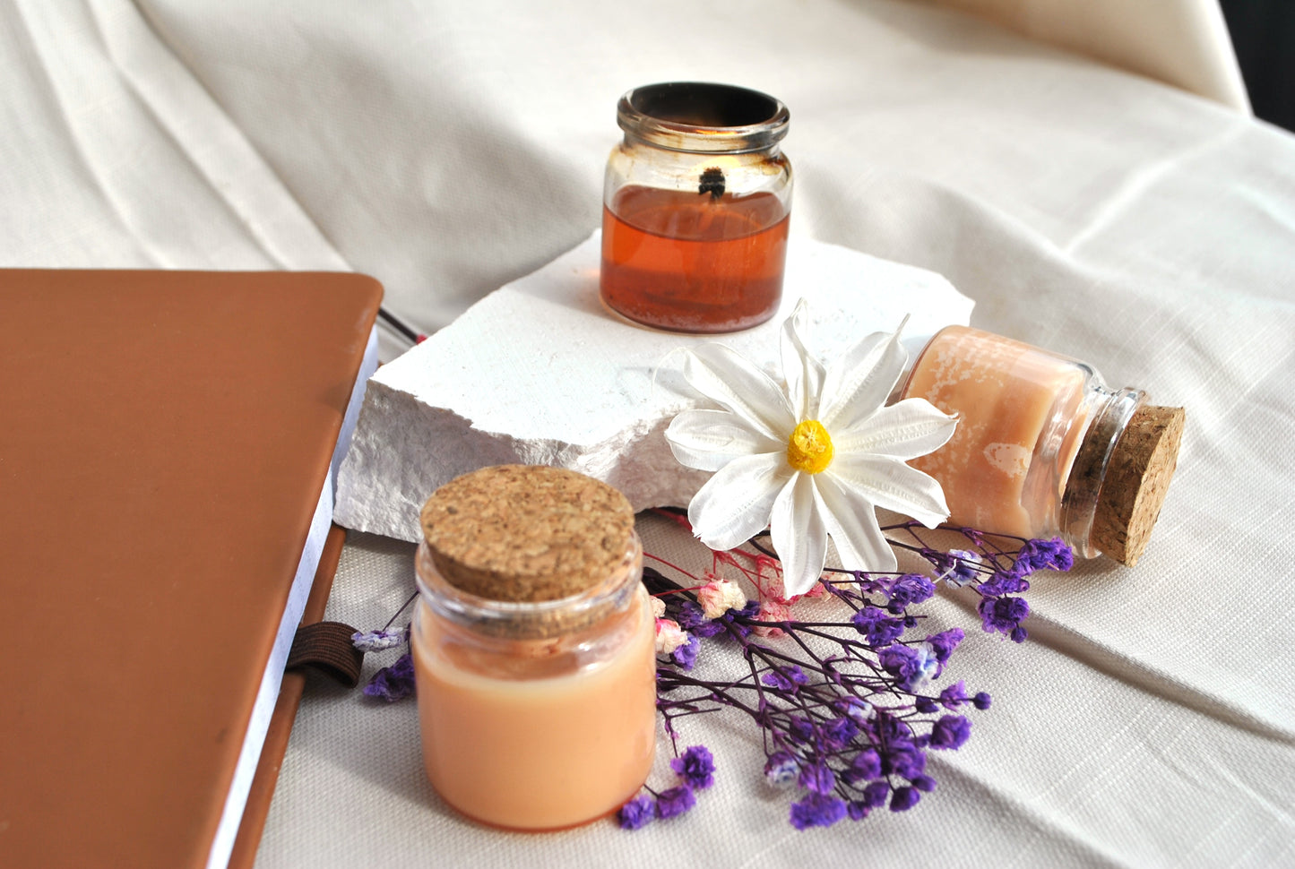 Jar candles with flowers on a white fabric background
