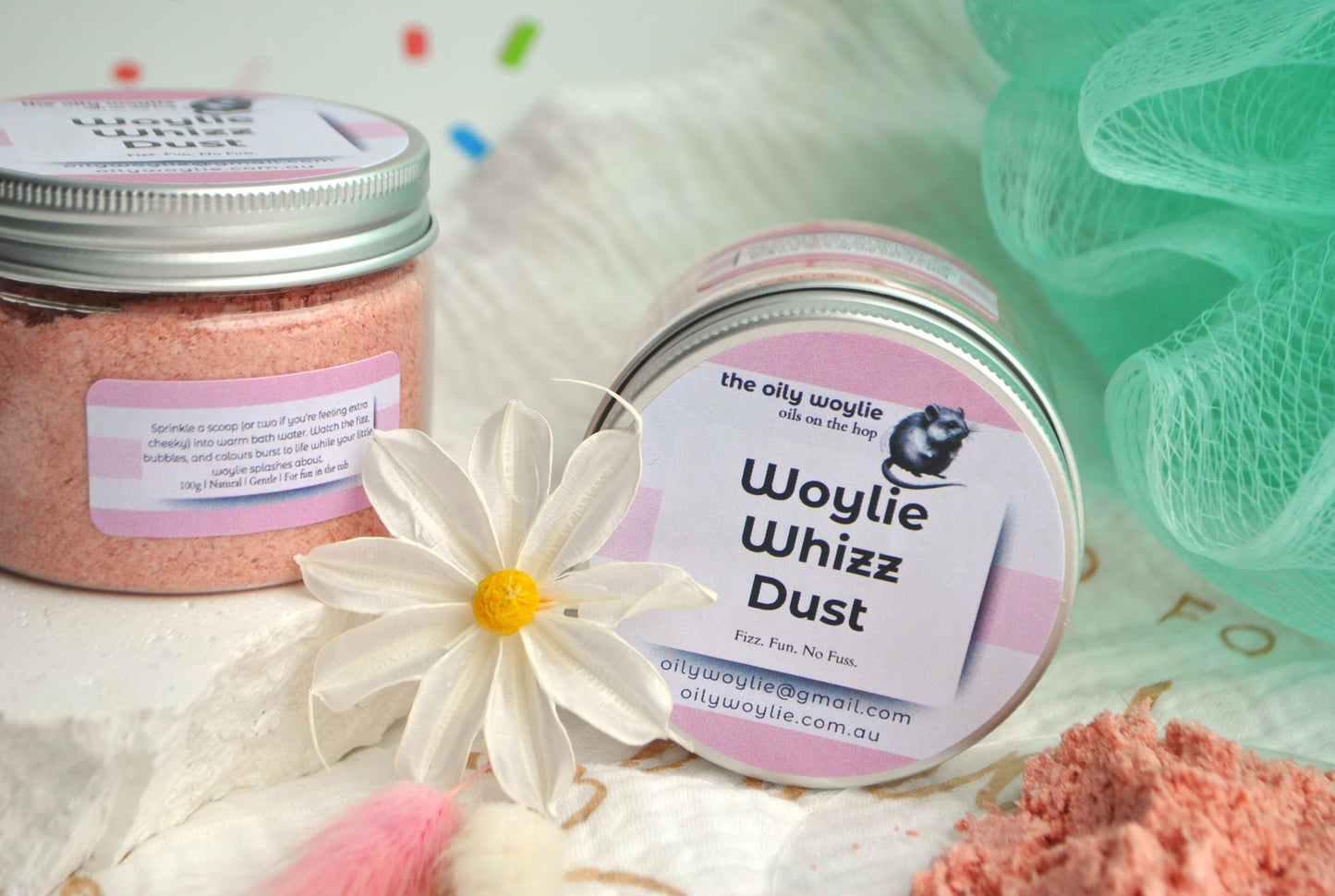 Two jars of Woylie Whizz Dust with a flower and green loofah in the background