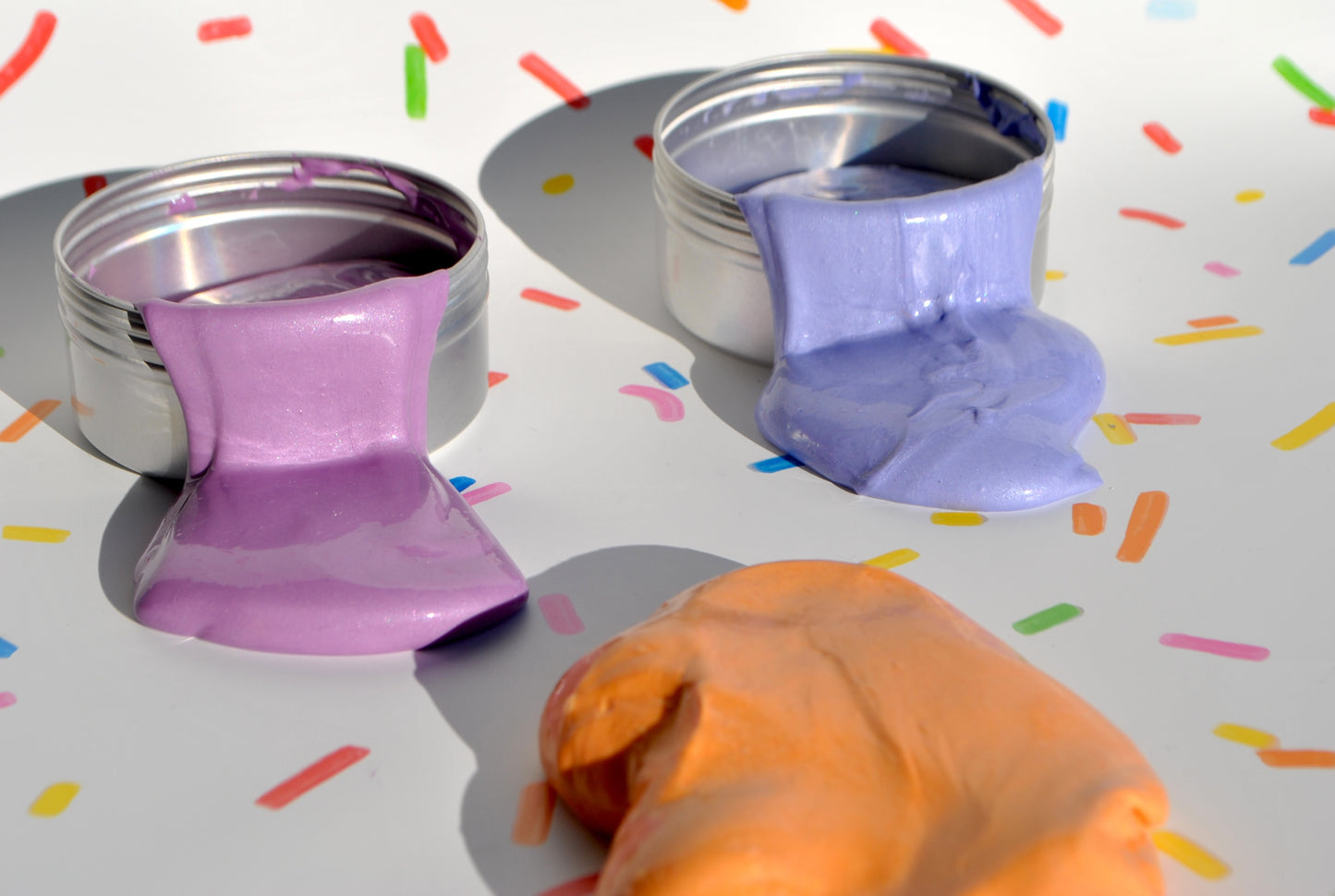 Two containers with purple and orange substances on a colorful confetti background