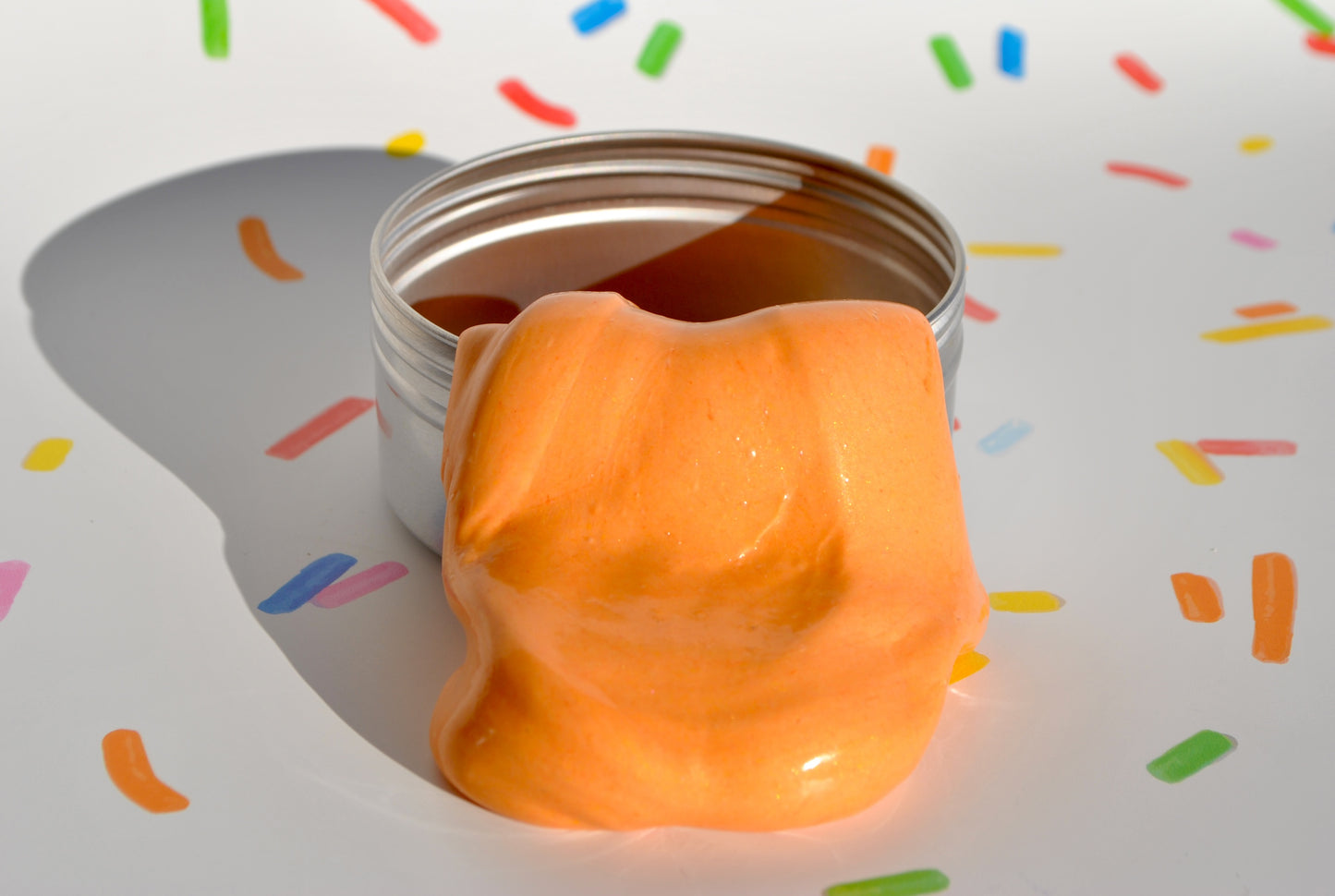 Orange slime oozing out of a silver container on a colorful confetti background
