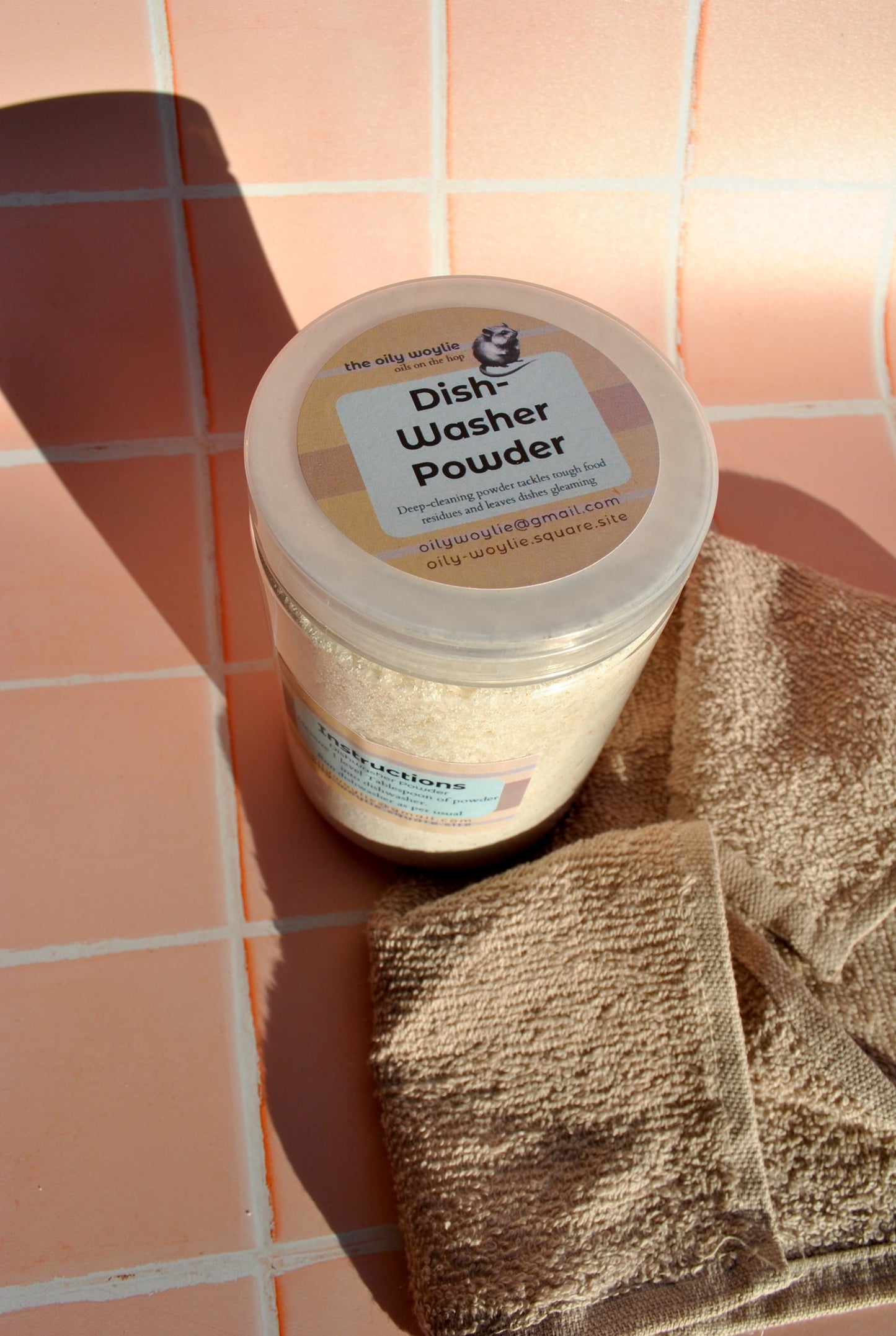Jar of dishwasher powder on a tiled floor with a brown towel.