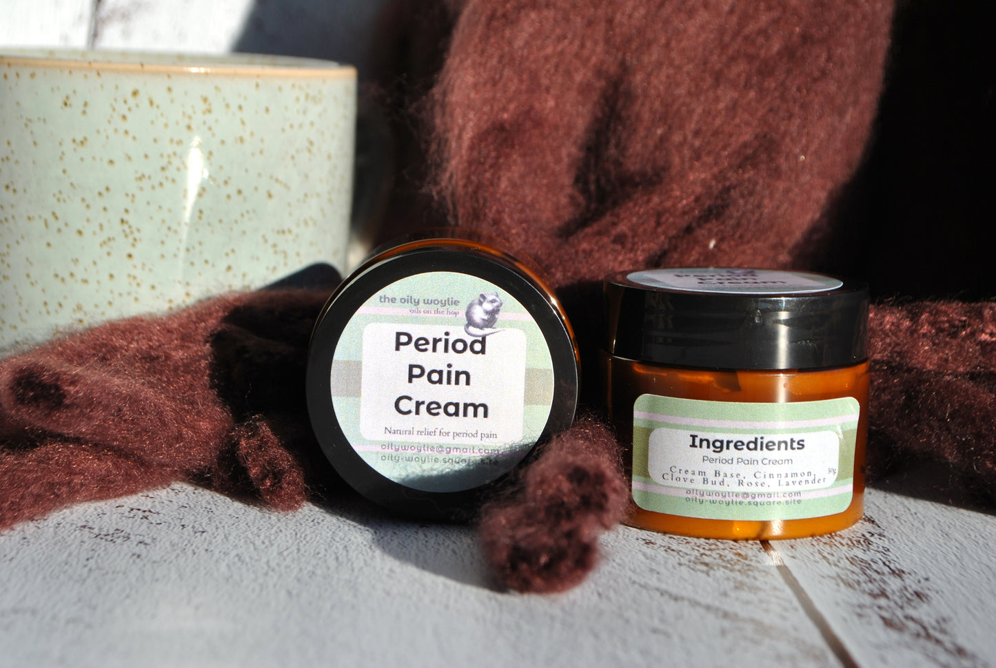 Two jars of Period Pain Cream on a wooden surface with a brown fabric background