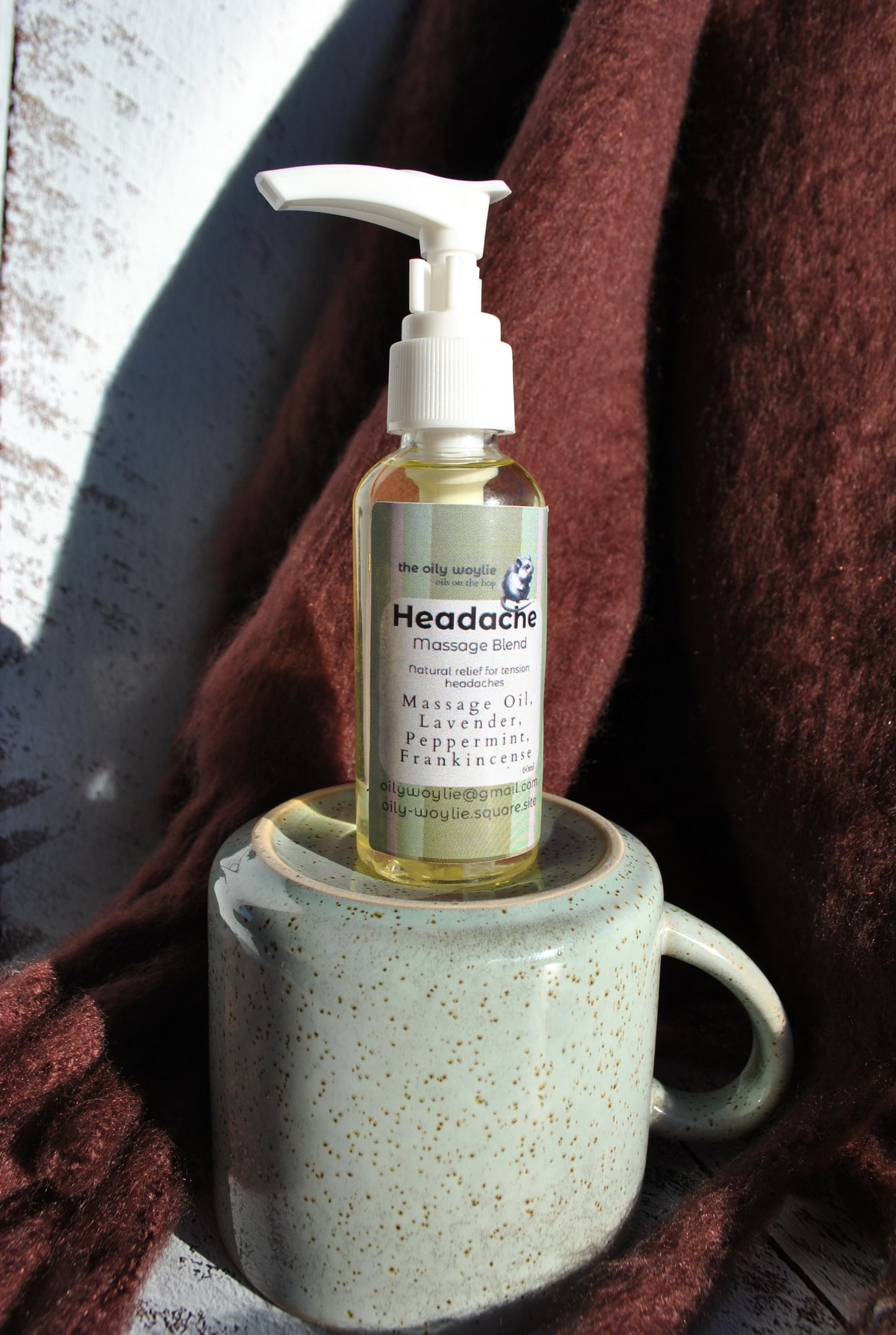Bottle of headache massage blend on a ceramic mug with a brown blanket in the background