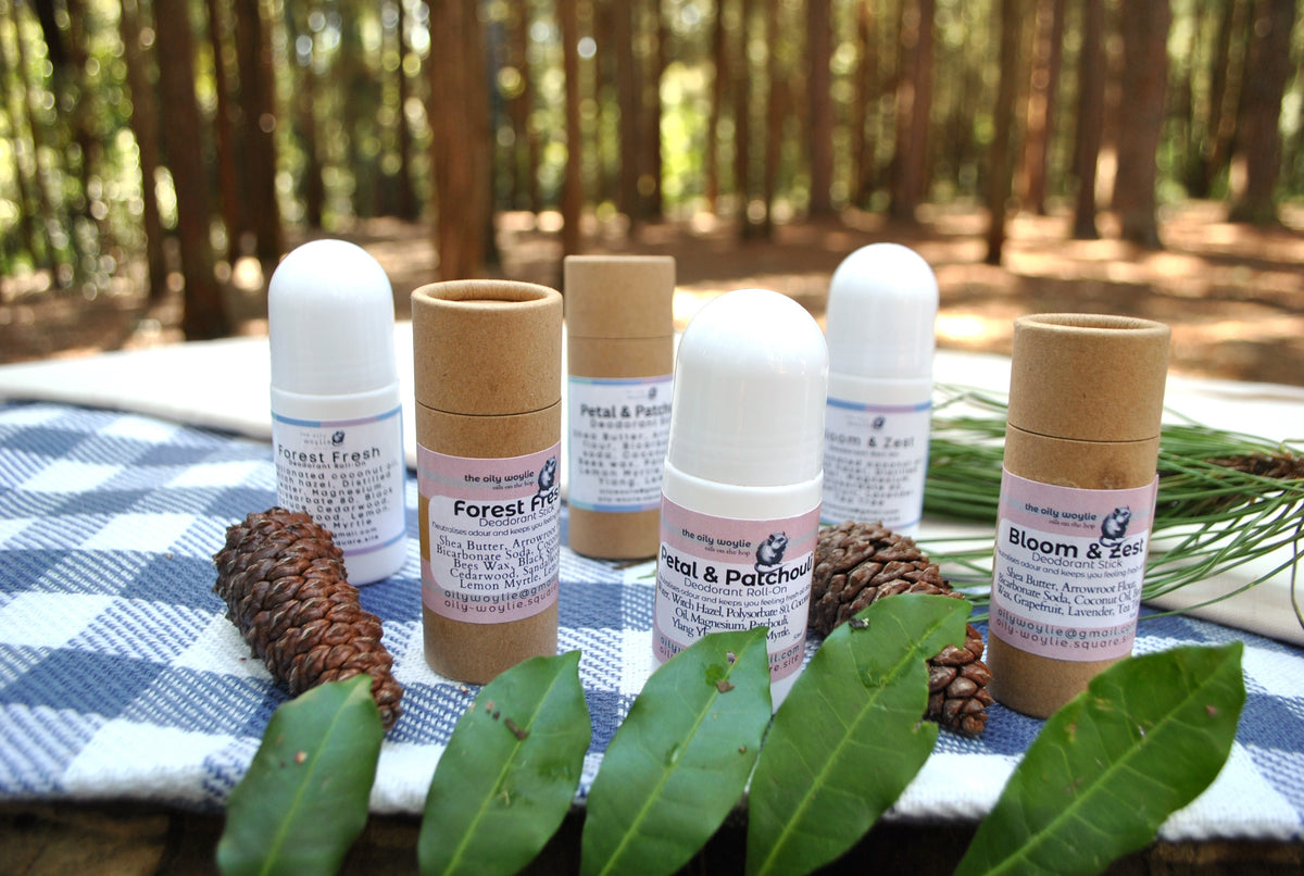 Natural deodorant family collection – Roll-On and Stick deodorants in Bloom & Zest, Forest Fresh, and Petal & Patchouli scents on a checkered cloth with a forest background