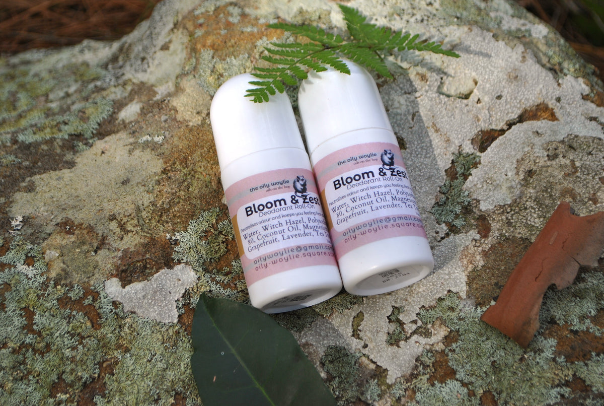 Deodorant Roll-On Bloom & Zest bottle, natural deodorant with citrus scent on a textured stone surface with green leaves.