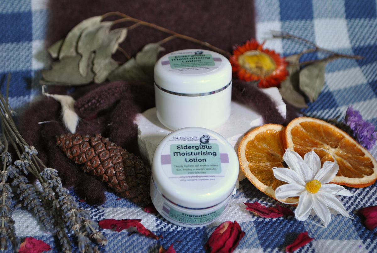 Elderglow Moisturising Lotion bottle, natural anti-aging lotion for soft and hydrated skin on a blue checkered tablecloth with dried flowers and oranges.