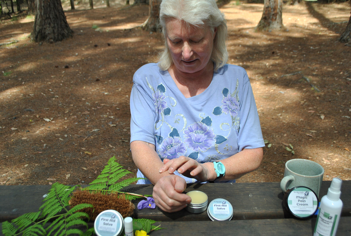 Close-up of hands applying The Oily Woylie First Aid Salve outdoors — soothing herbal ointment for bites, scratches, and minor burns.