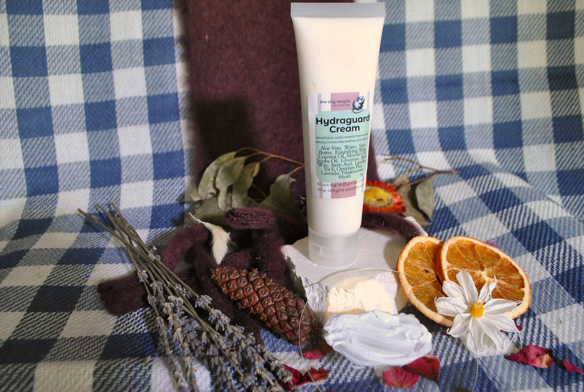 Hydraguard Cream tube, natural moisturising cream for dry skin protection on a checkered fabric background with dried oranges and flowers.