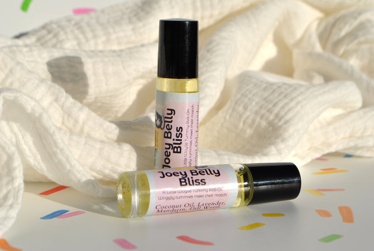 Joey Belly Bliss essential oil blend in a roller bottle, natural tummy support for kids in front of baby wrap