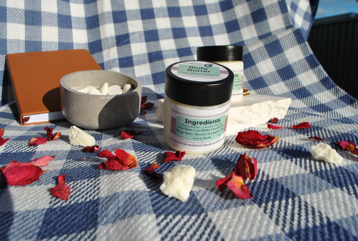 Lemon Myrtle Body Butter jar, natural moisturising body cream with lemon myrtle scent on a checkered fabric background with flowers and a notebook.