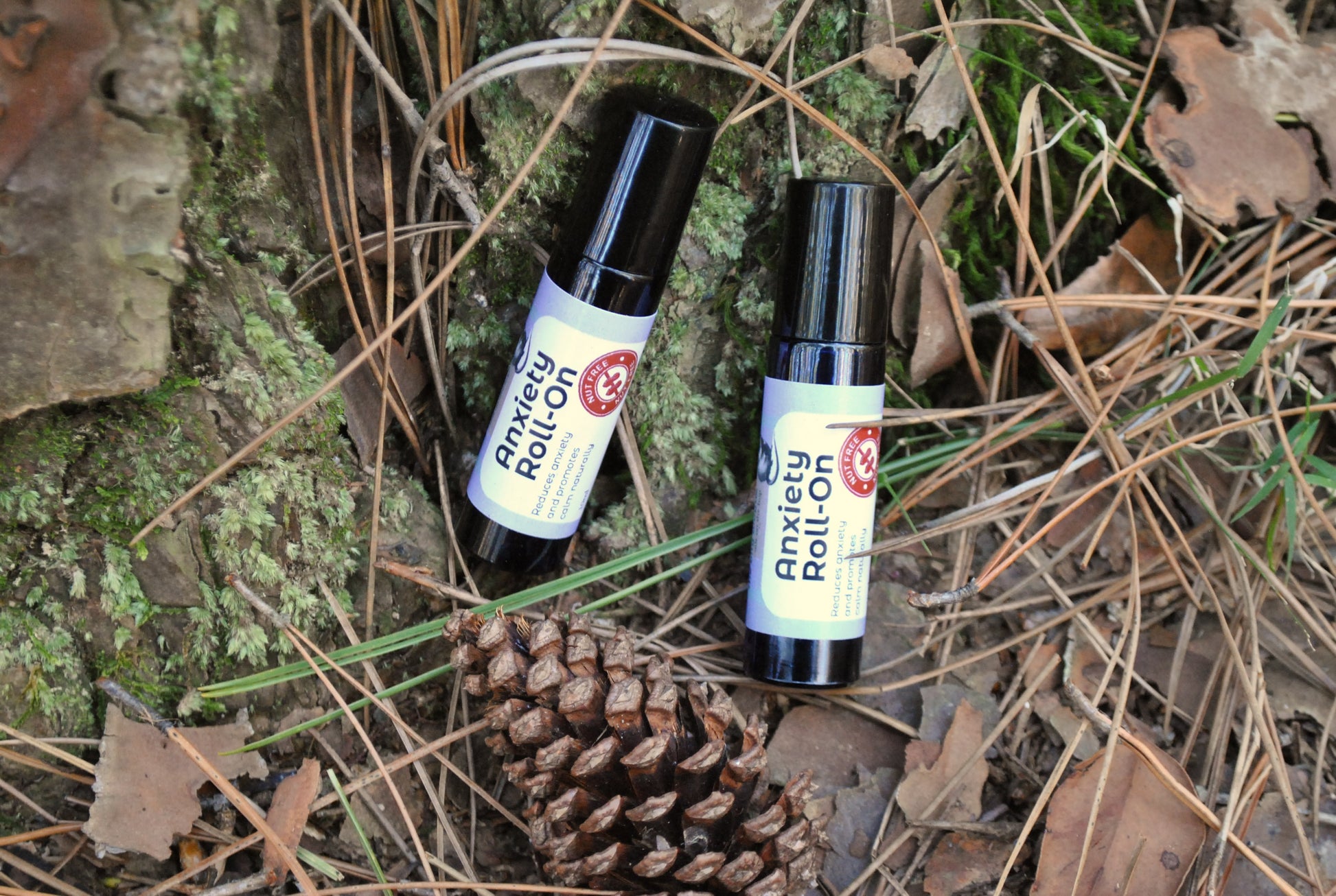 Two Anxiety Roll-on bottles on a natural background with pine cones and leaves.
