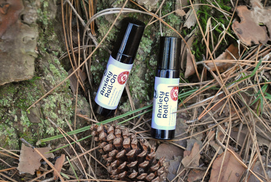 Two Anxiety Roll-on bottles on a natural background with pine cones and leaves.