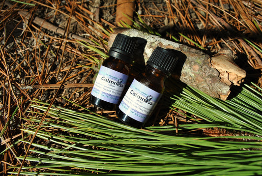 Two bottles of 'Calmness' on a natural background with pine needles and branches.