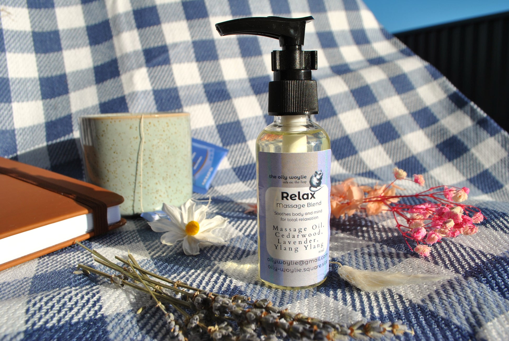 Massage oil bottle labeled 'Relax' on a checkered fabric background with flowers and a notebook.