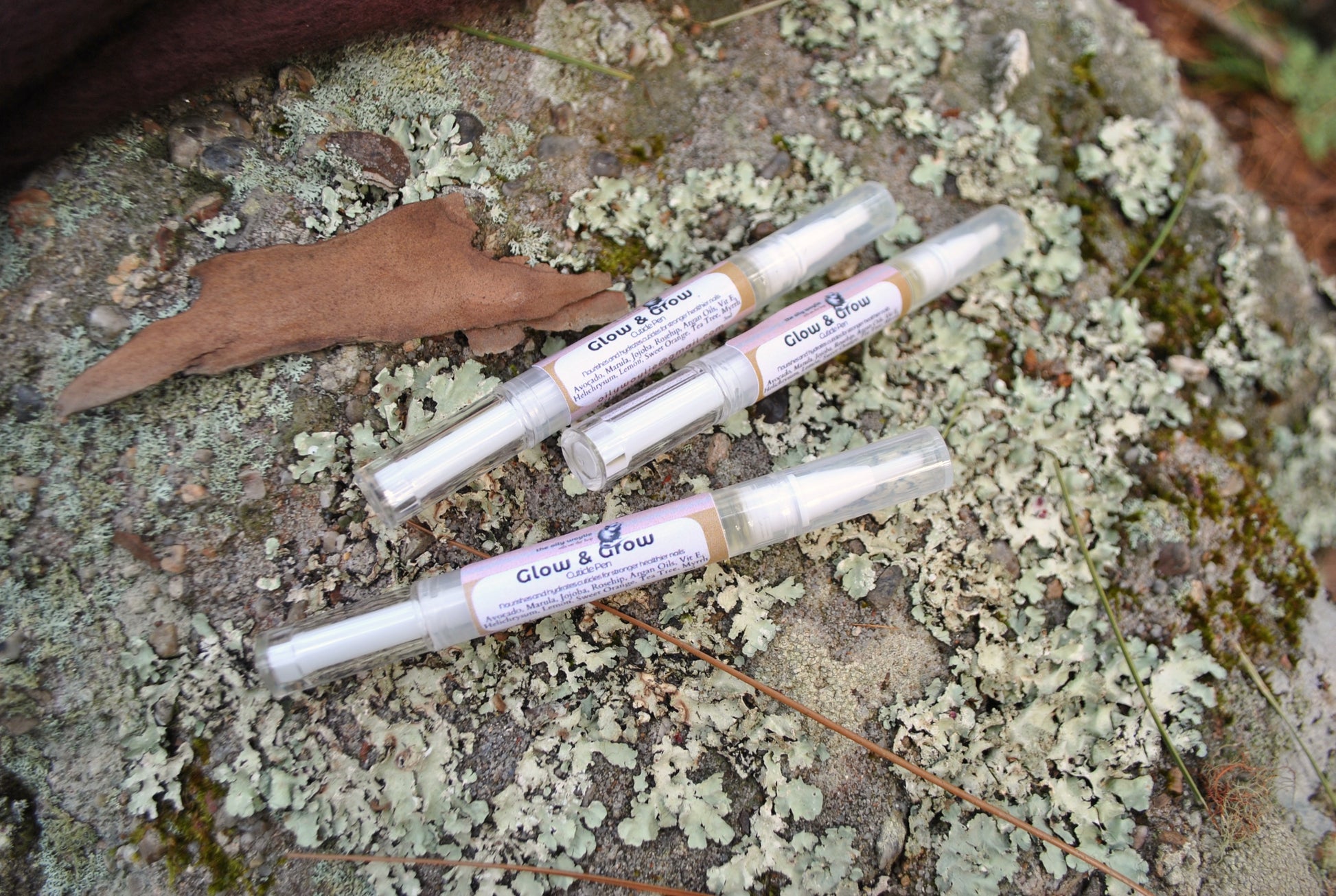Four small tubes labeled 'Glow & Brow' on a textured stone surface with lichen.