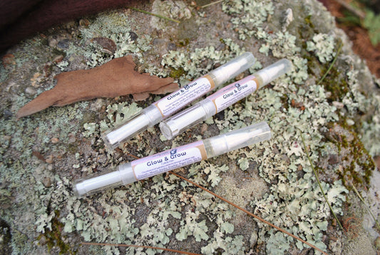 Four small tubes labeled 'Glow & Brow' on a textured stone surface with lichen.