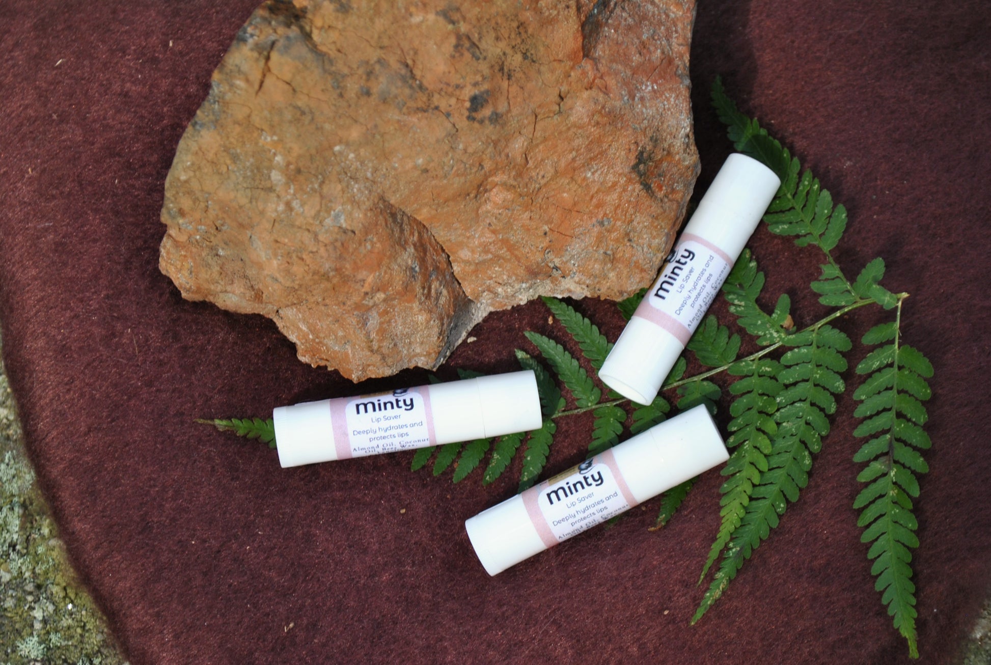 Three lip balm tubes labeled 'minty' on a rock with green leaves