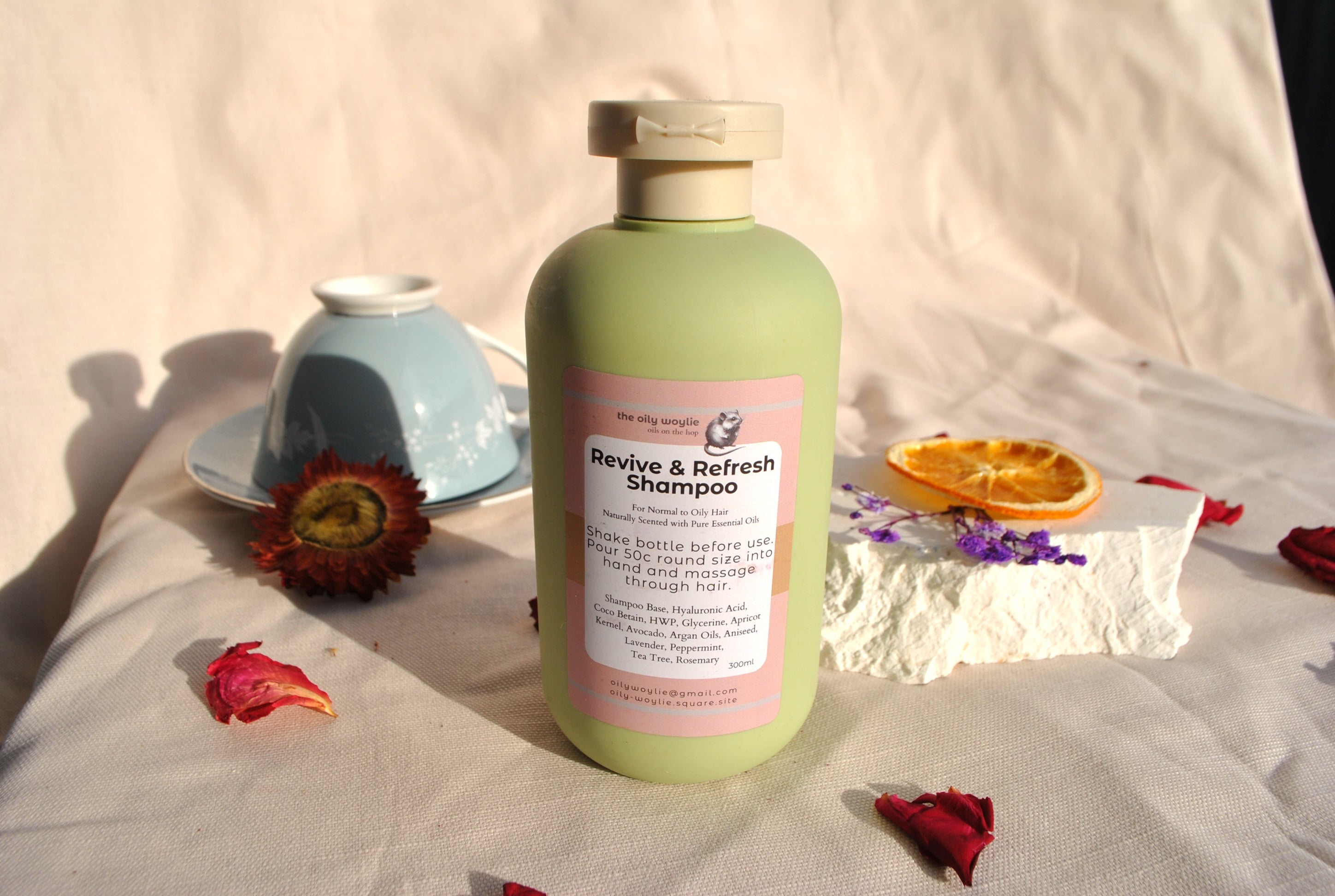 Green shampoo bottle with pink label on a light fabric background with flowers and a bowl.