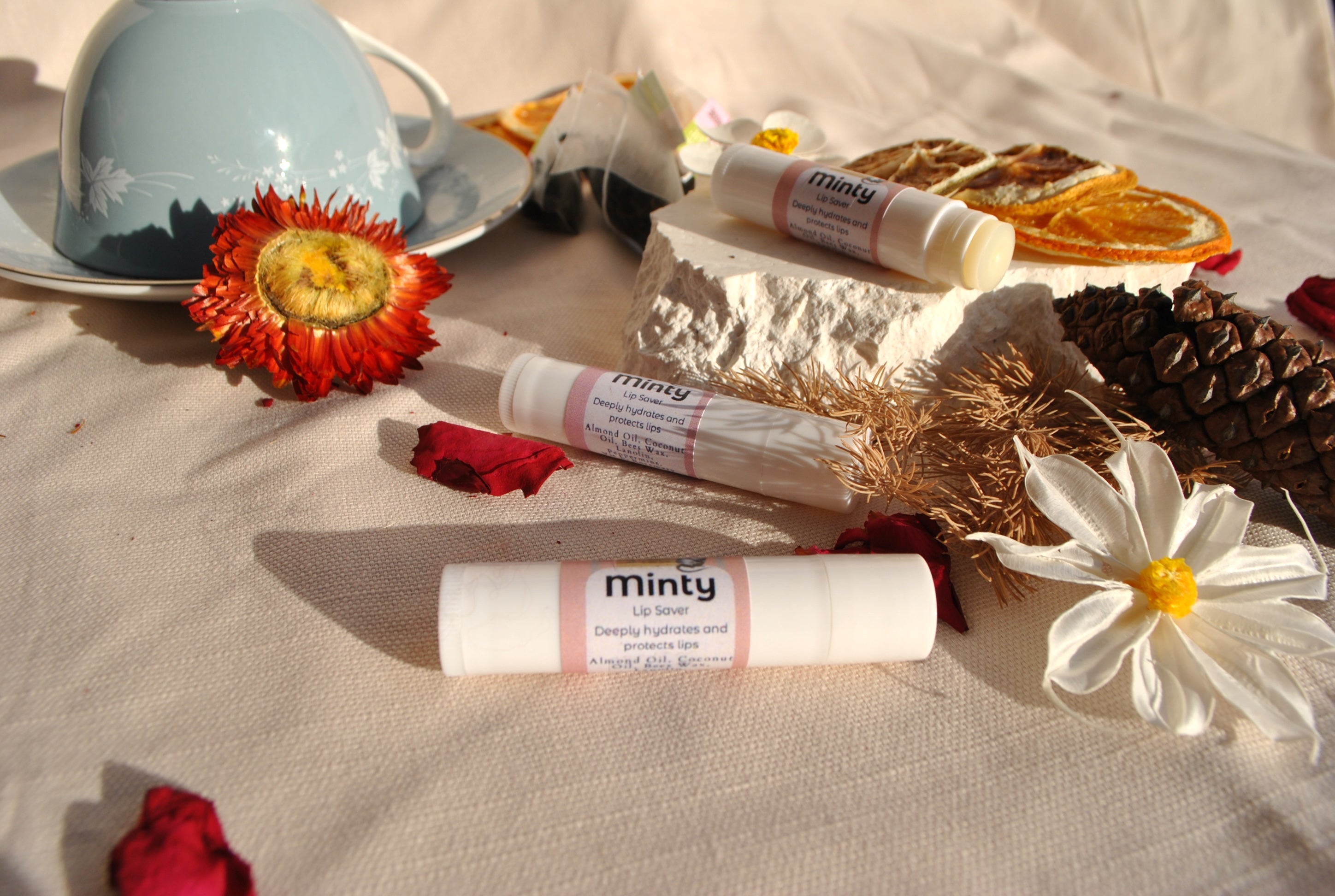 Lip balm tubes with decorative flowers and a teacup on a textured surface