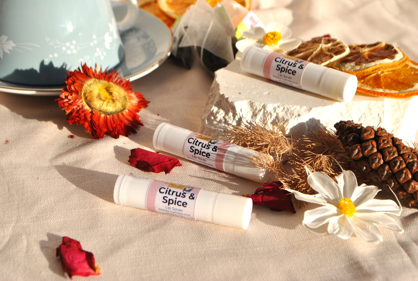 Lip balms labeled 'Citrus & Spice' on a table with flowers and a teacup.