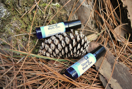 Two bottles of 'Sleep Roll On' on a pine cone and wooden surface with pine needles.
