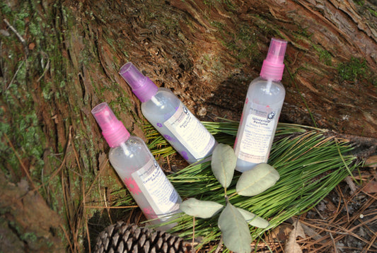 Three spray bottles with pink nozzles on a leafy branch against a natural background.