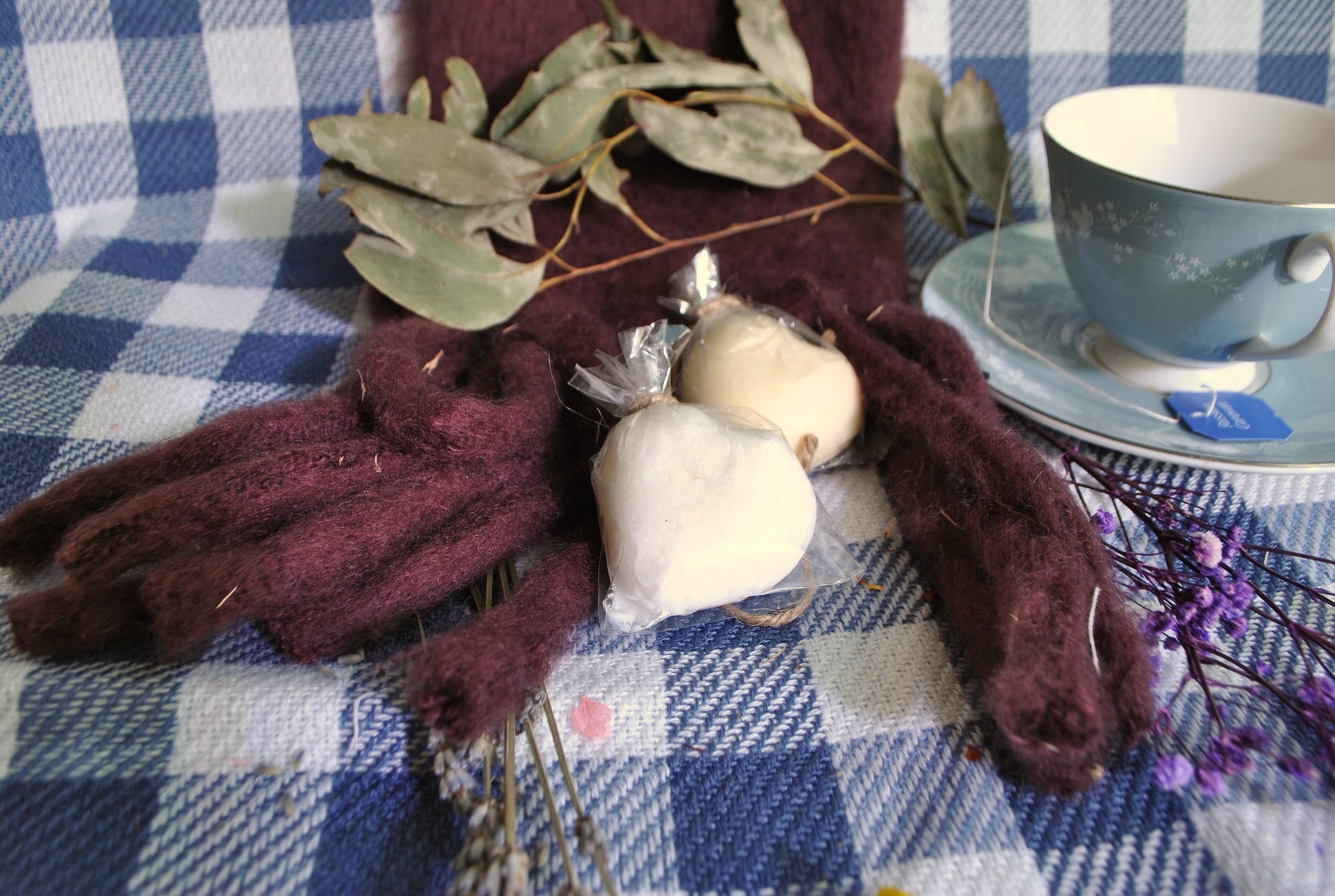 Decorative items including a teacup, scarf, and flowers on a checkered tablecloth.