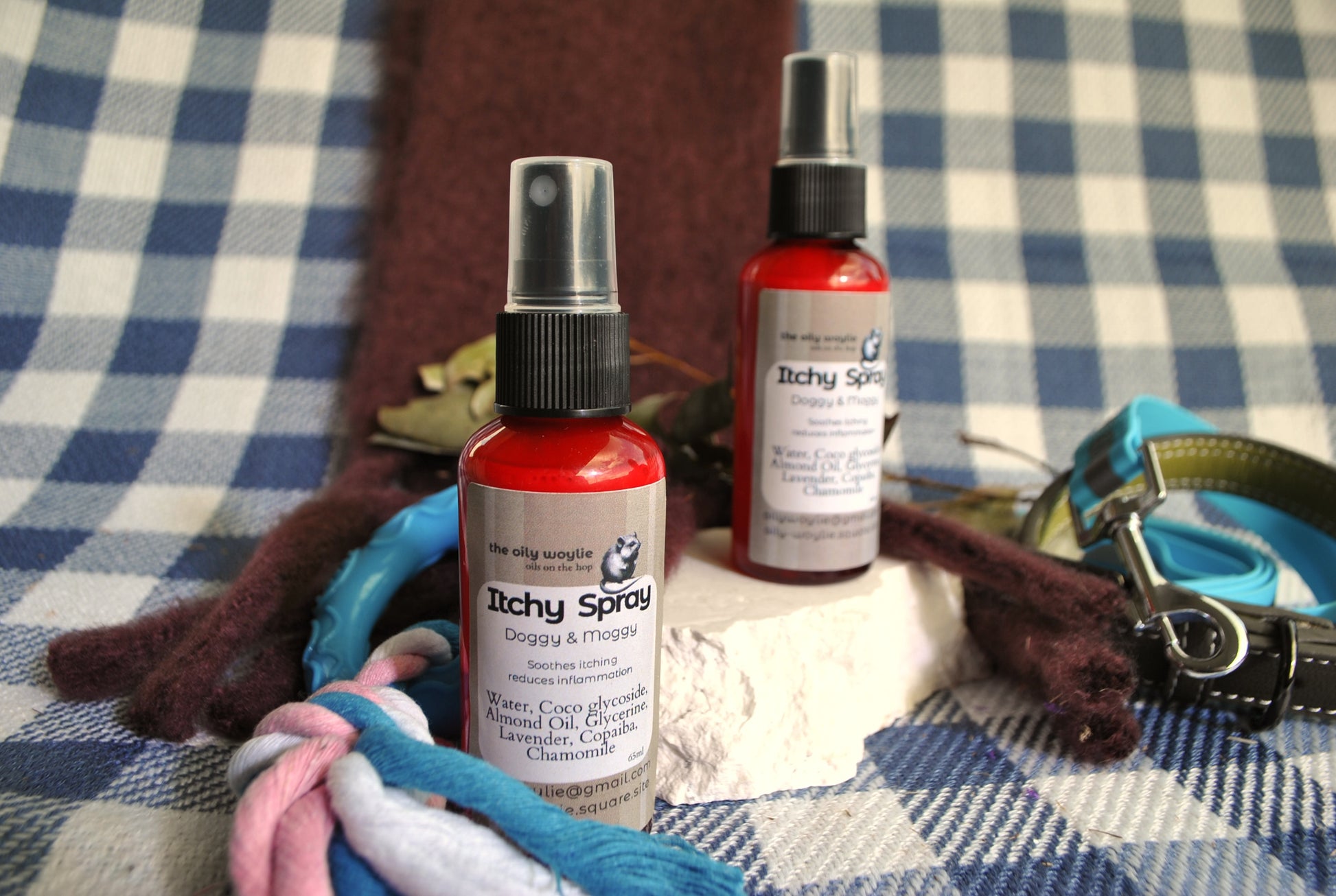Two bottles of 'Itchy Spray' on a checkered fabric background with pet accessories.